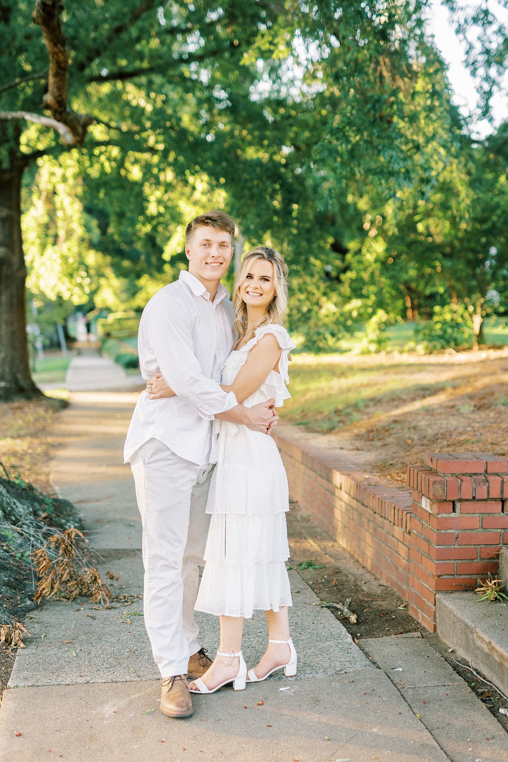 engaged couple stands on sidewalk hugging in white outfits