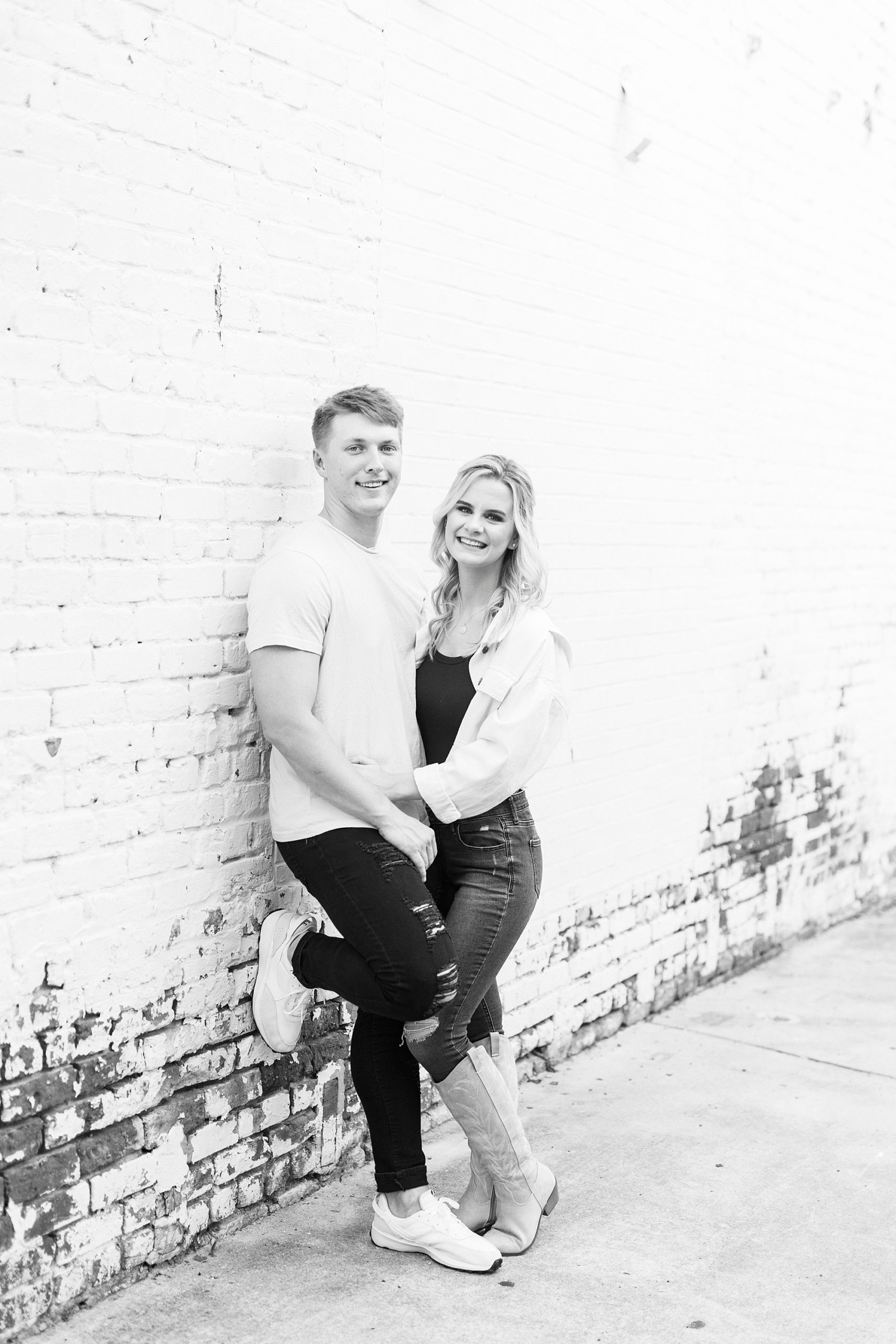 engaged couple leans against white washed wall in Downtown Concord 
