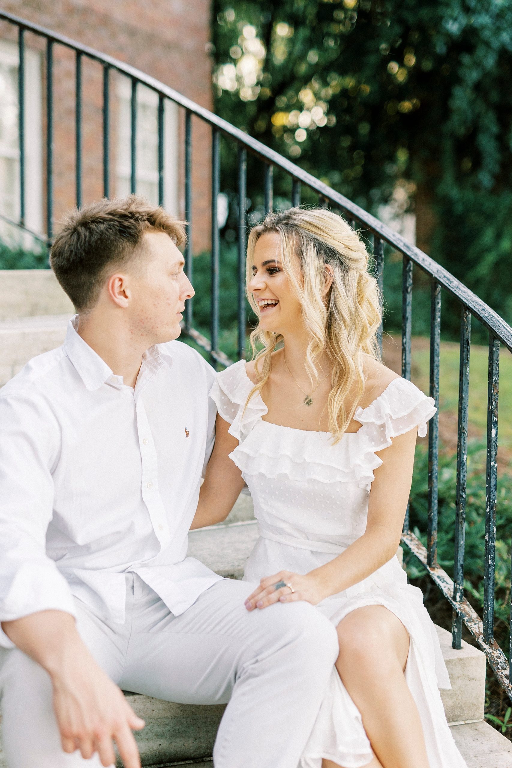 engaged couple sits on steps laughing together
