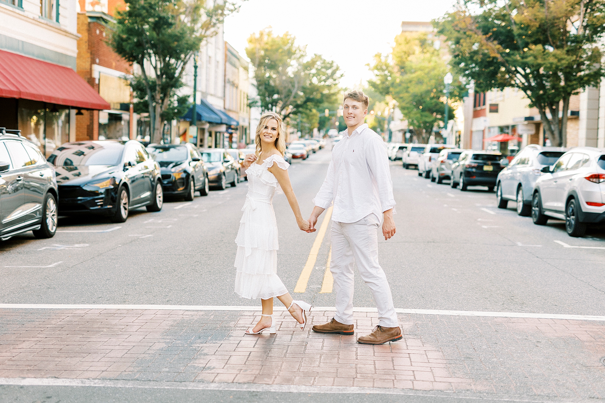 woman leads fiancee through crosswalk during Downtown Concord engagement portraits