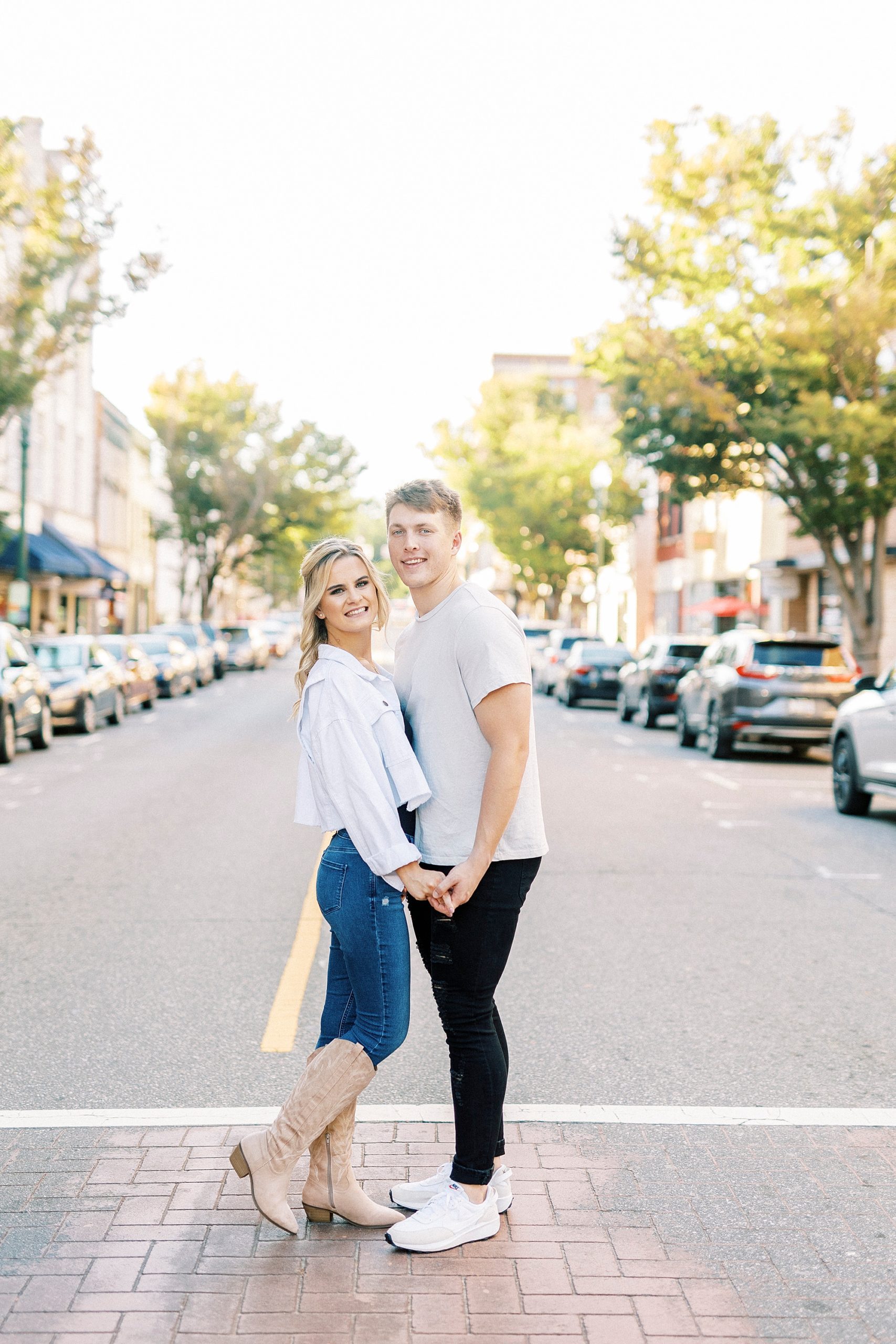 engaged couple holds hands in crosswalk during Downtown Concord engagement portraits