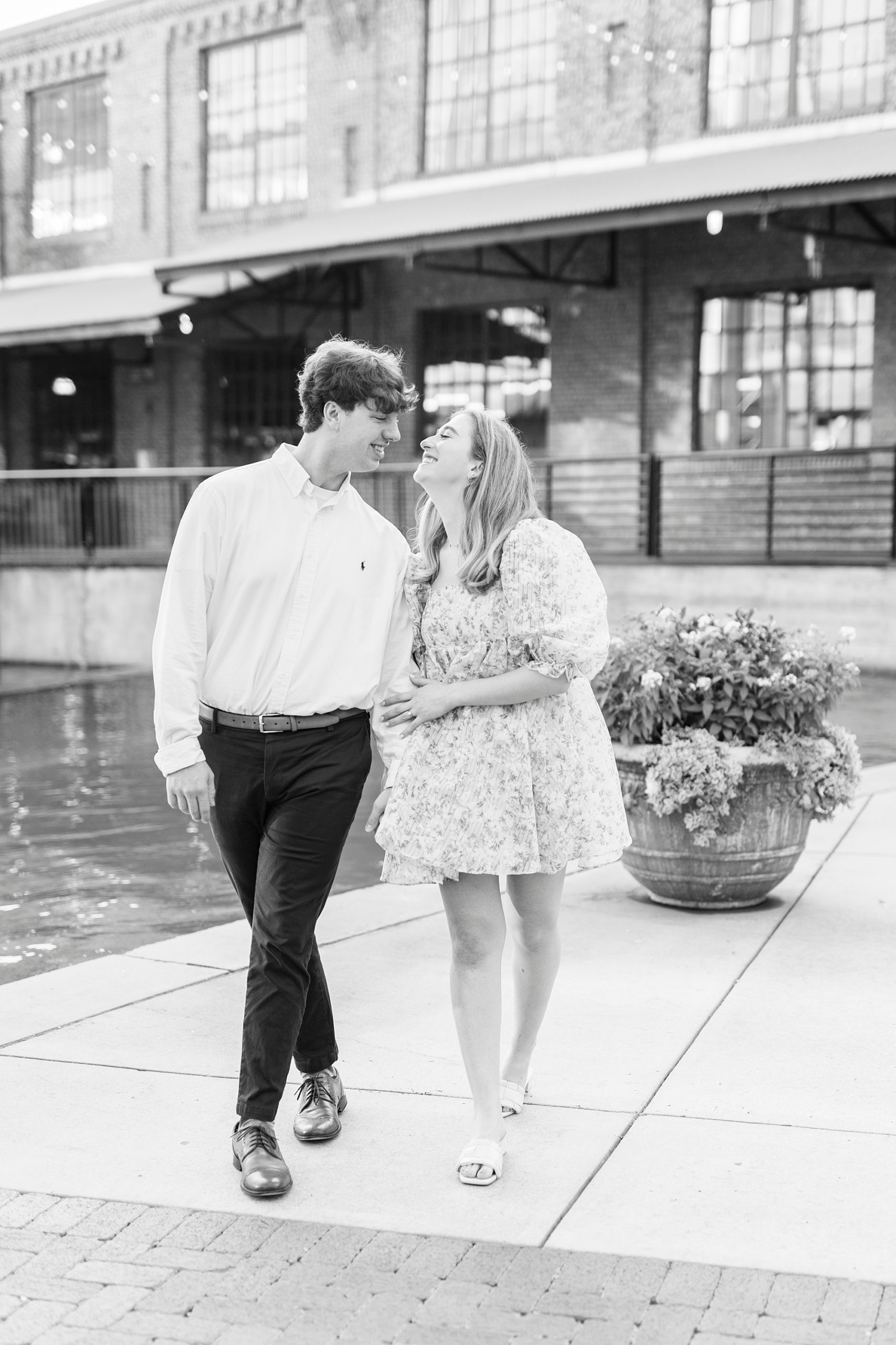 black and white portrait of engaged couple walking by water at American Tobacco Campus