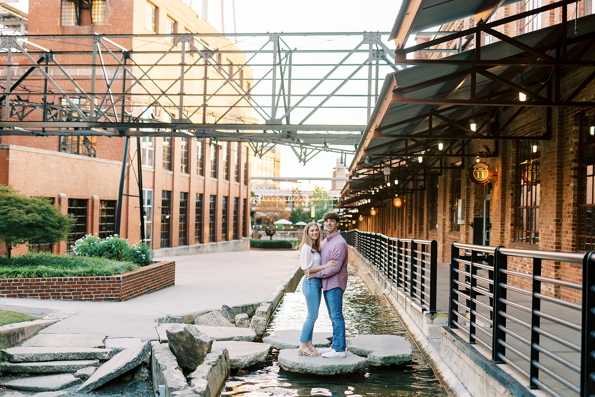 engaged couple stand son rocks in water outside American Tobacco Campus