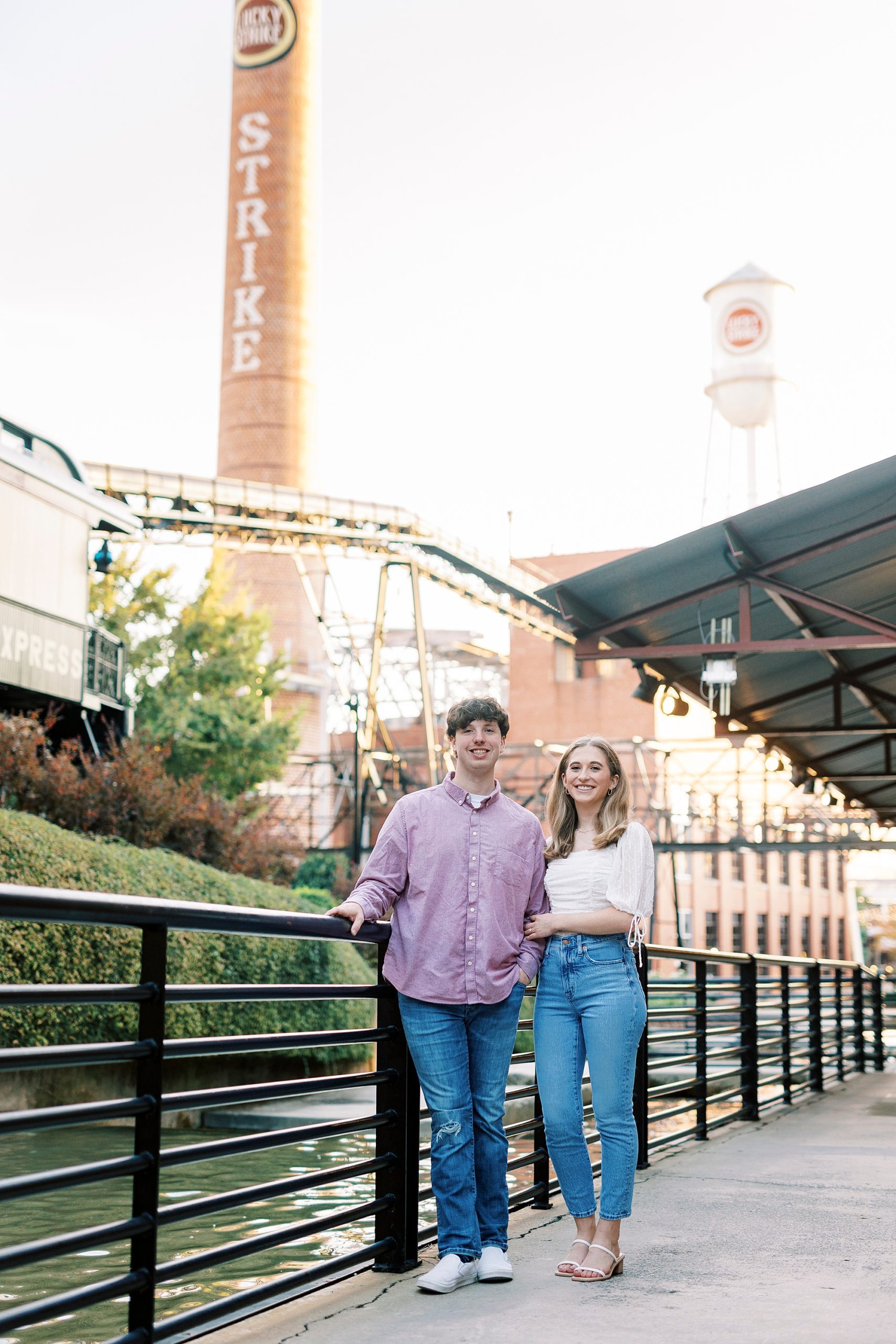 engaged couple poses along waterway with American Tobacco Campus behind them
