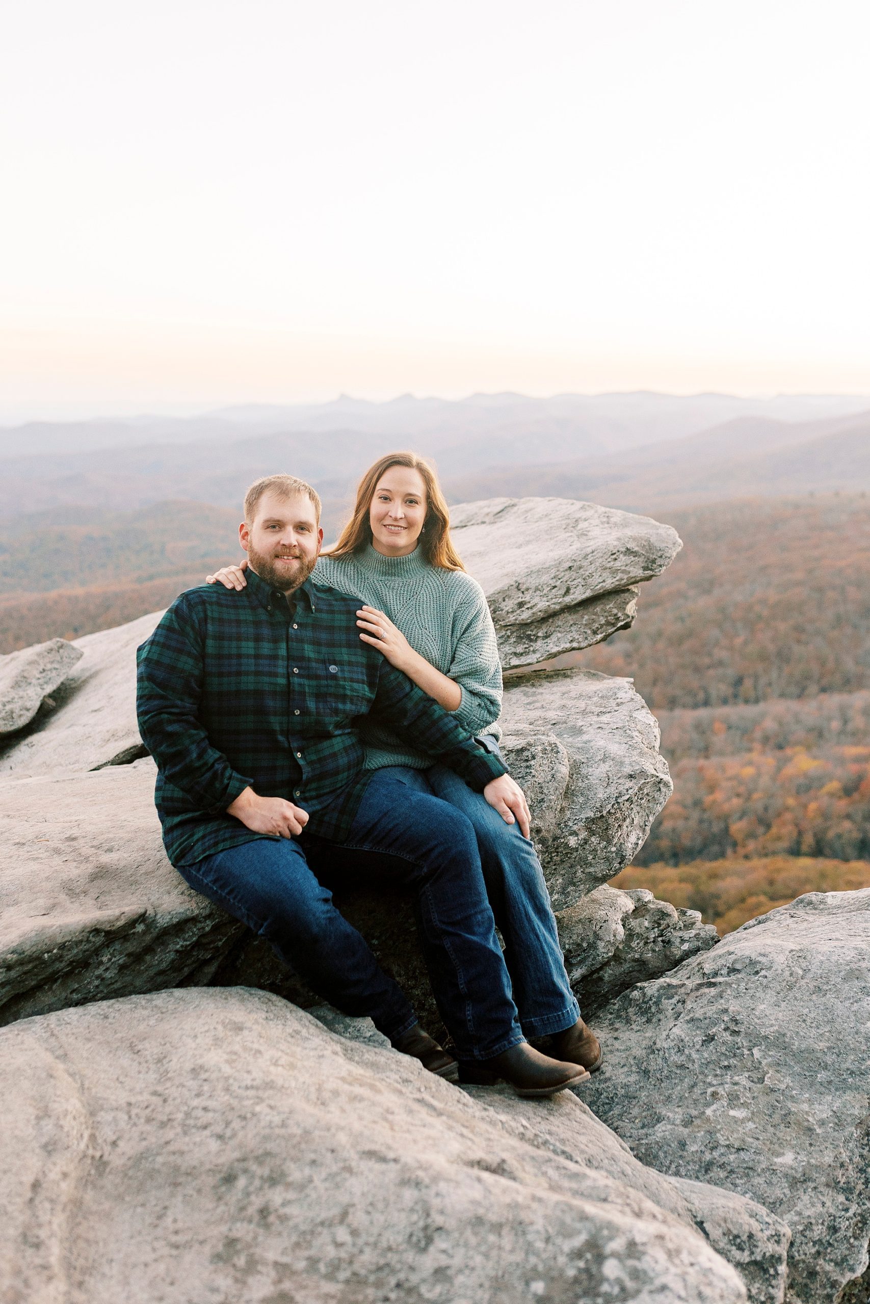 engaged couple sits on rocks at Rough Ridge