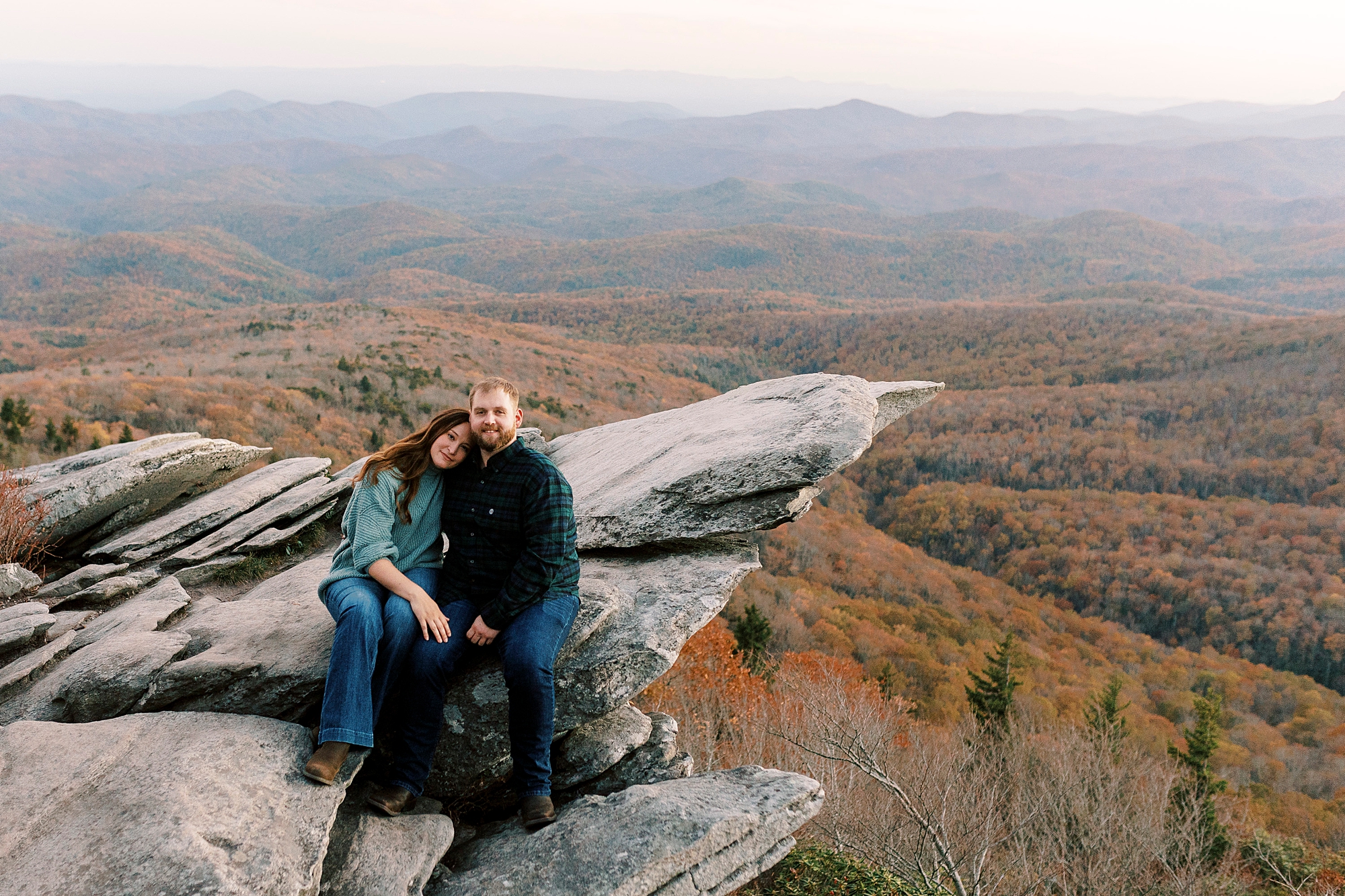 engaged couple sits on rocks of Rough Ridge in the Blue Ridge Parkway