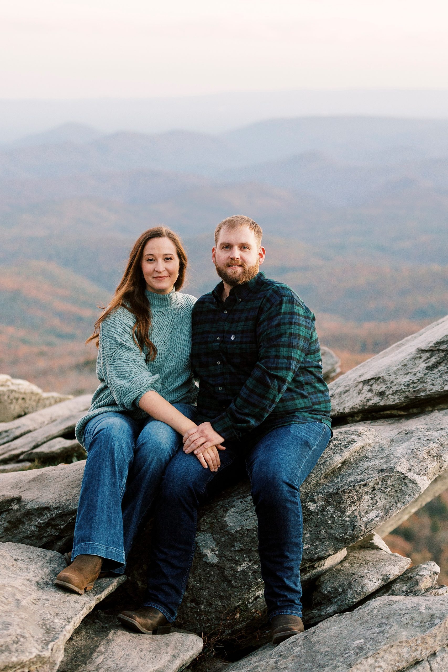 couple sits on Rough Ridge in the Blue Ridge Parkway with mountains behind them 