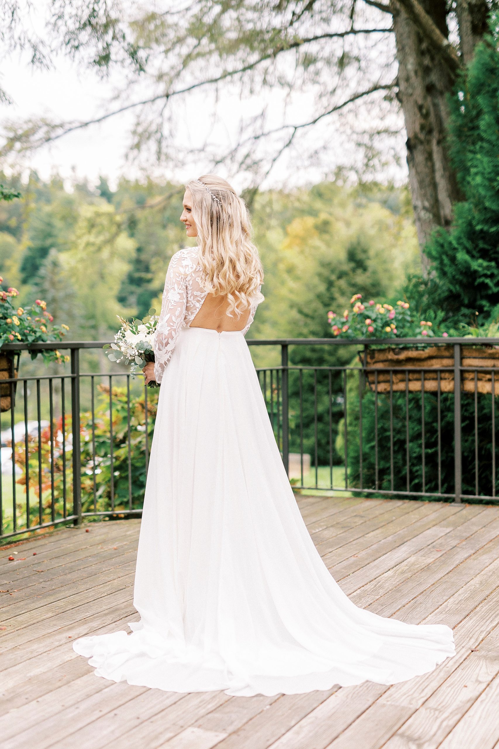 bride stands on balcony in wedding gown with lace sleeves and open back at Chetola Resort