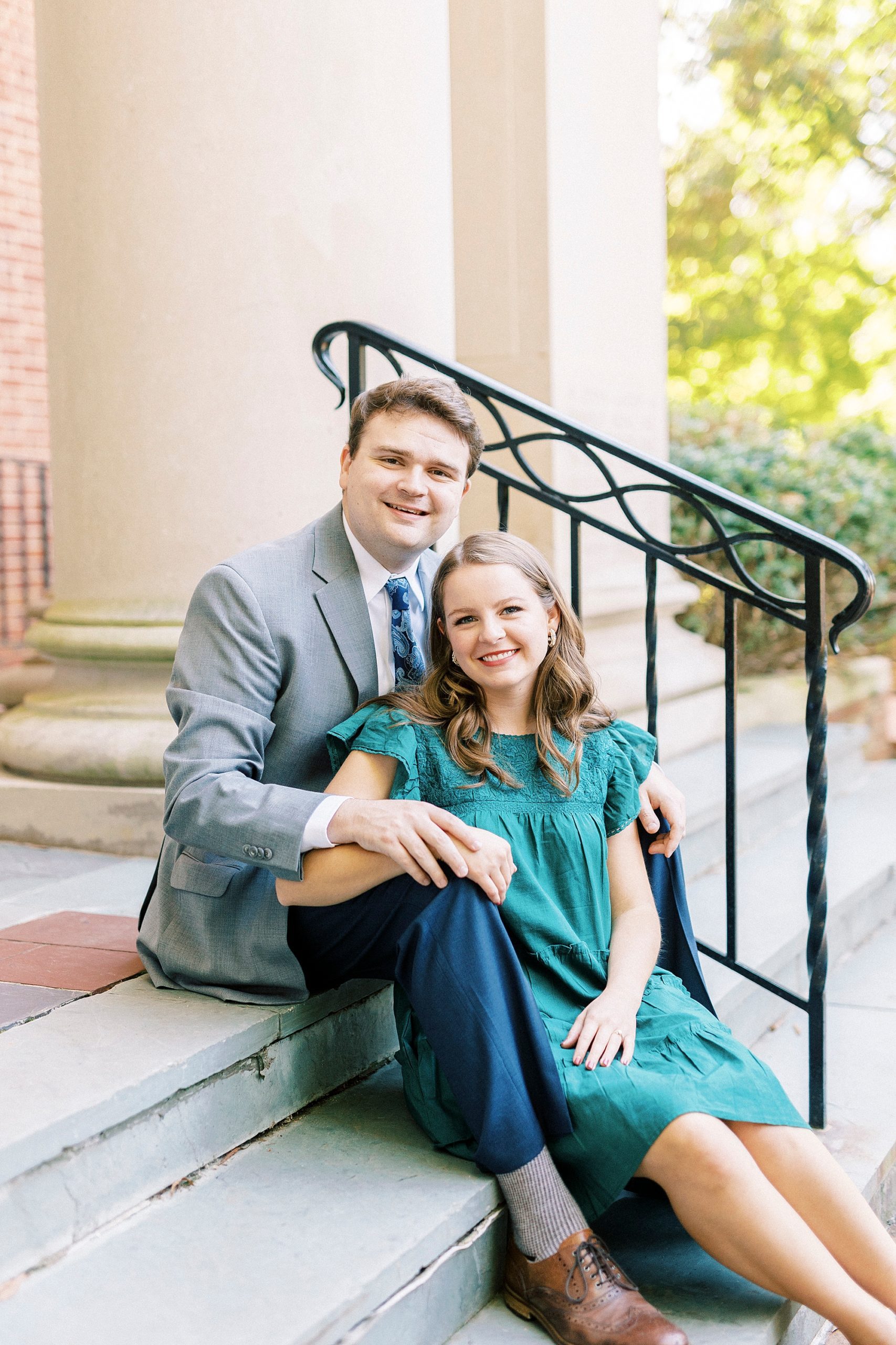 bride sits in front of groom during portraits n steps in Downtown Davidson