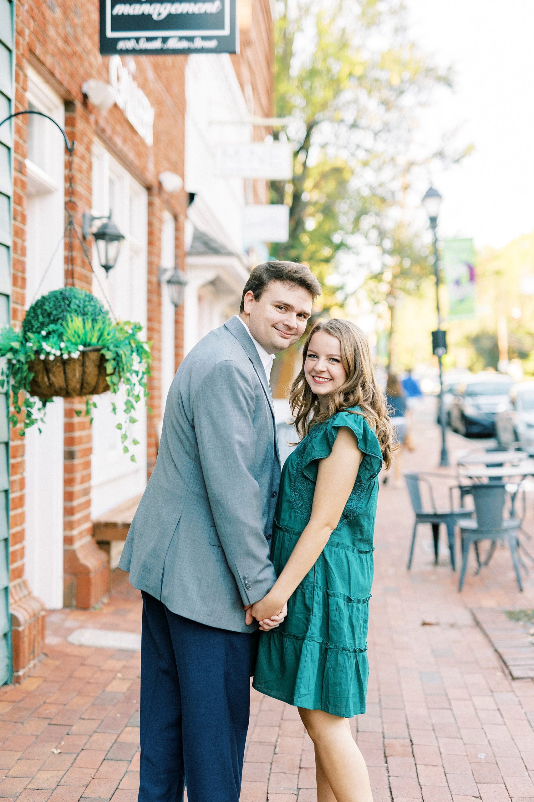 bride and groom hold hands leaning heads together on sidewalk in Downtown Davidson