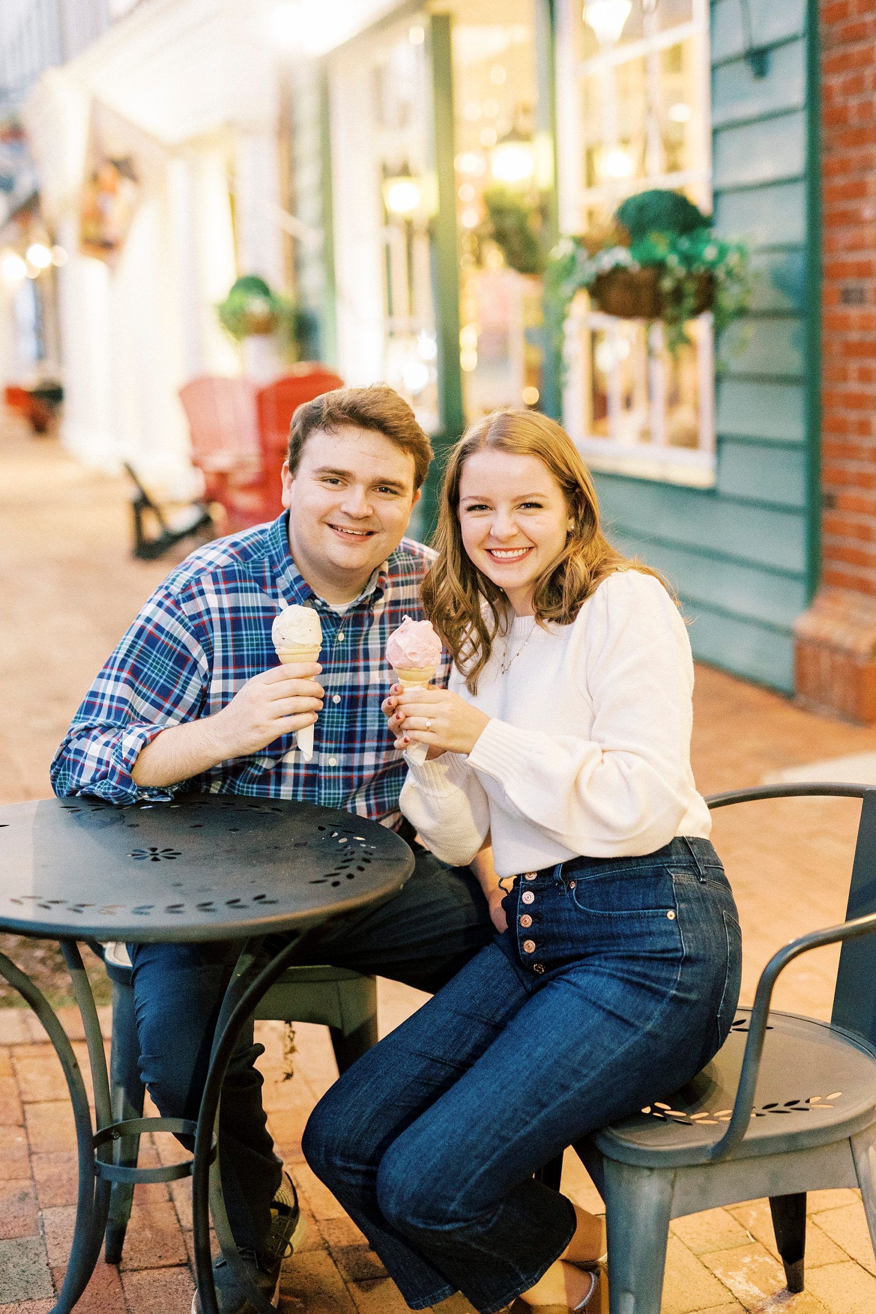 engaged couple sits outside ice cream shop during Downtown Davidson engagement portraits