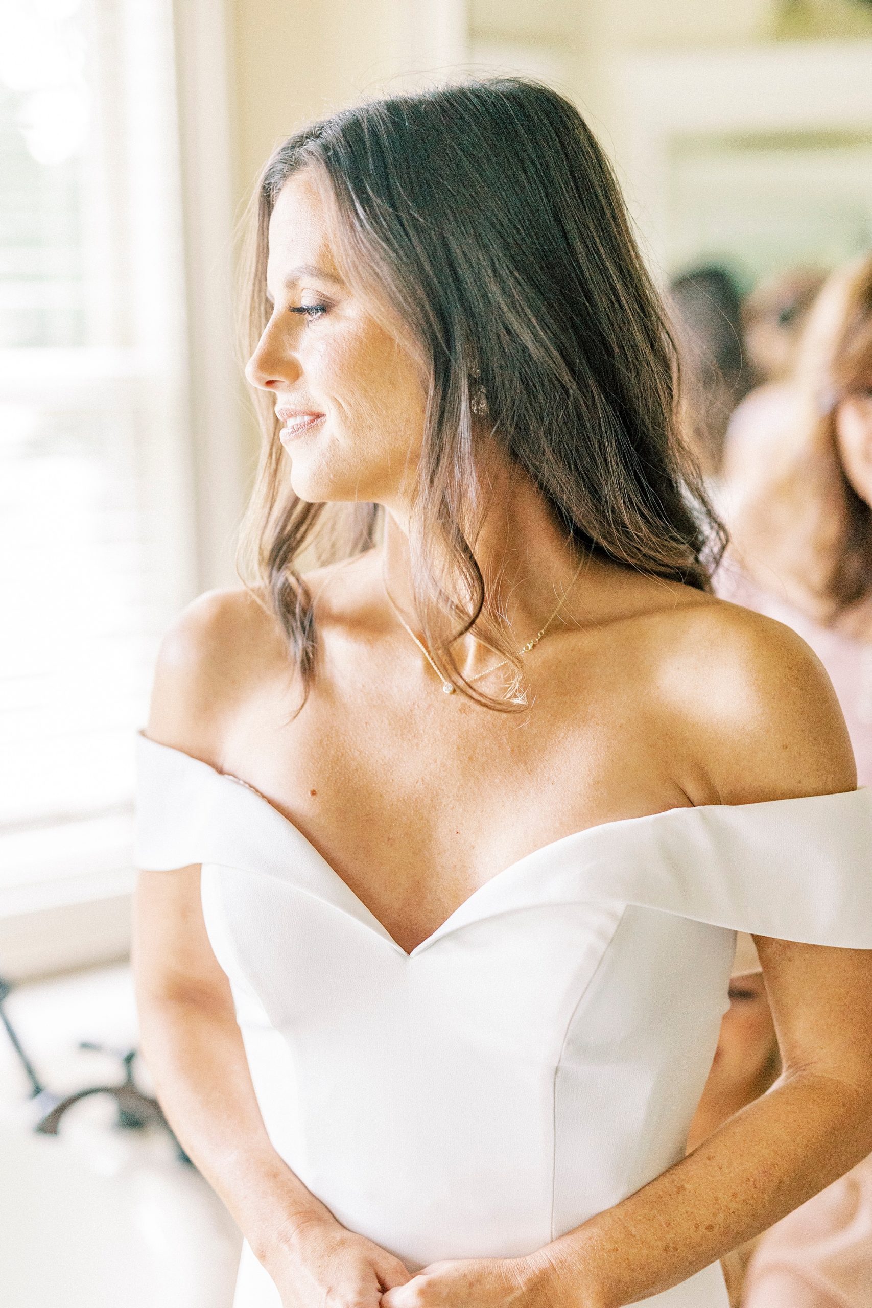 bride in off-the-shoulder gown looks over shoulder at Lake Norman