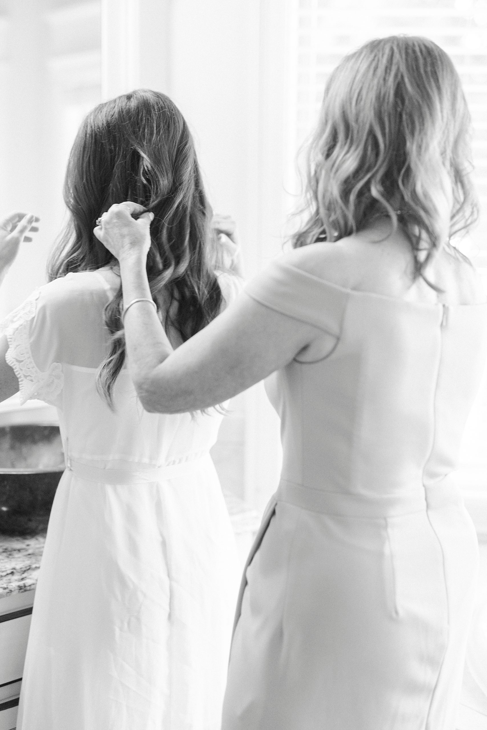 mother helps bride with wedding gown and hair