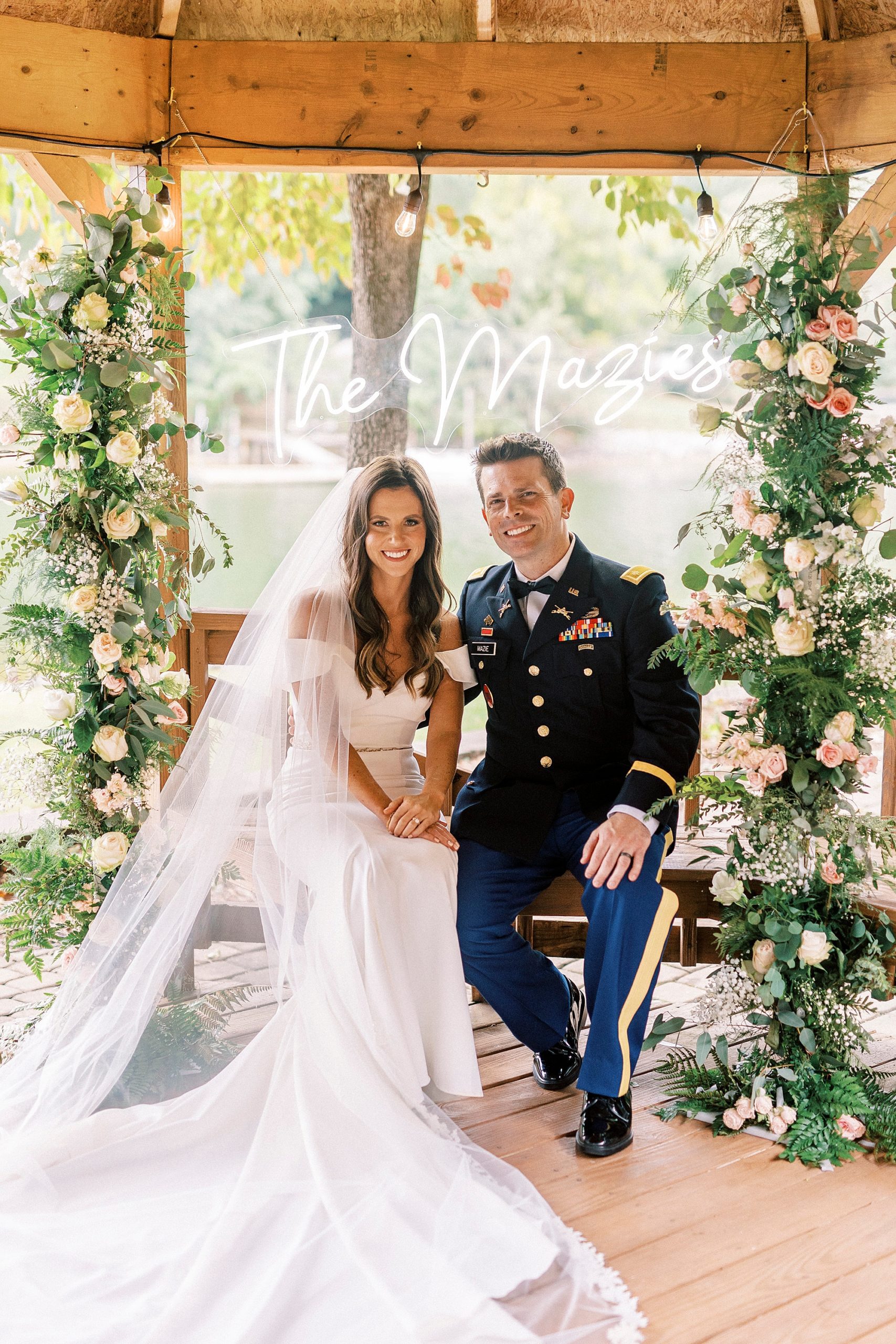 newlyweds sit on wooden bench surrounded by floral arbor at Lake Norman