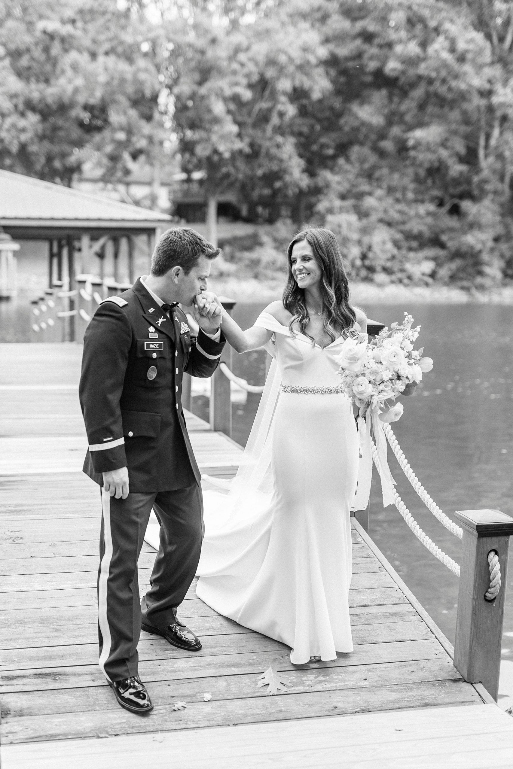 groom kisses bride's hand during photos on wooden dock