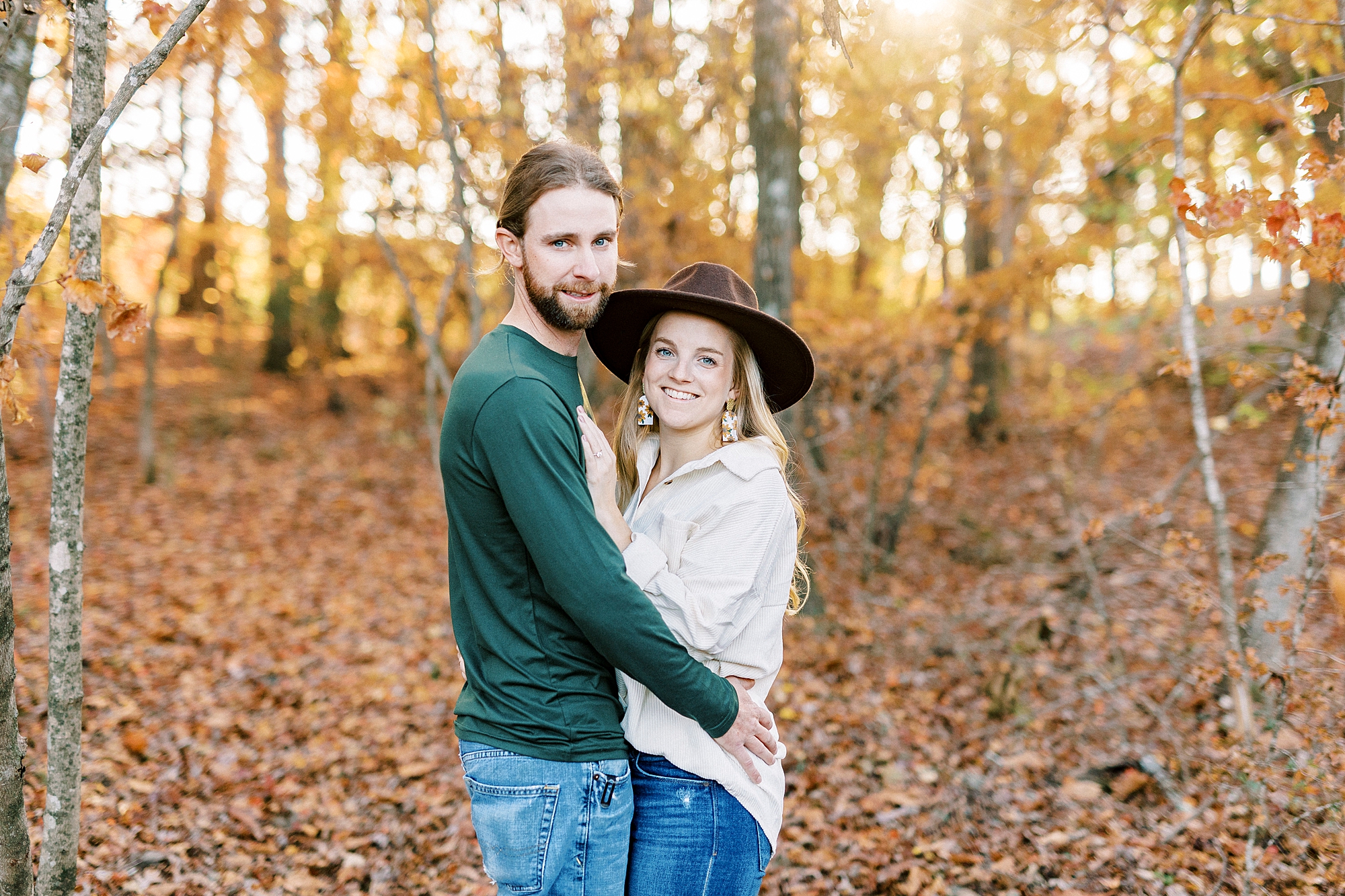 woman in ivory sweater and hat hugs fiancee during chic fall engagement session
