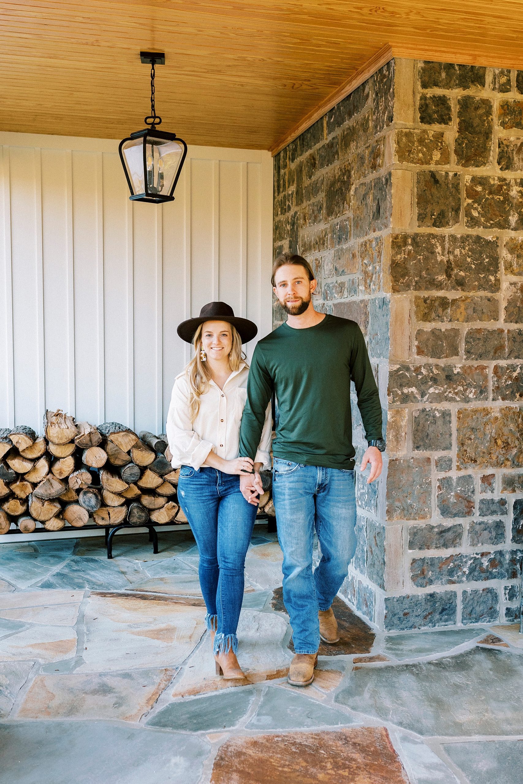 bride and groom hug by stone wall during chic fall engagement session at home
