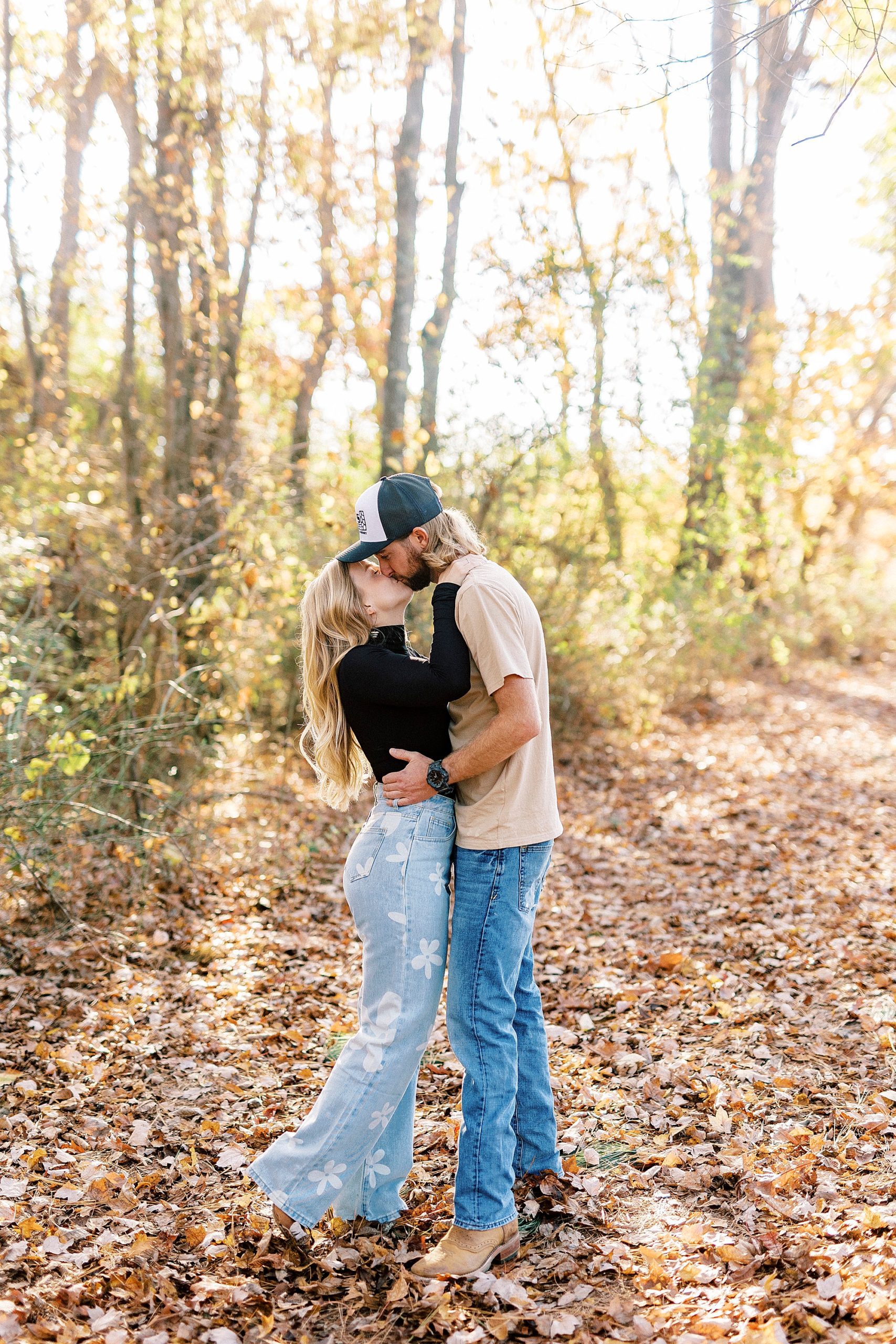 bride and groom hug and kiss in woods during chic fall engagement session