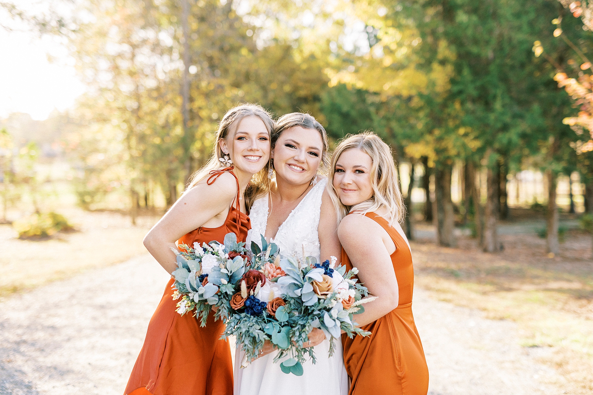 bride smiles hugging bridesmaids in burnt orange gowns on walkway at Bella Terra 