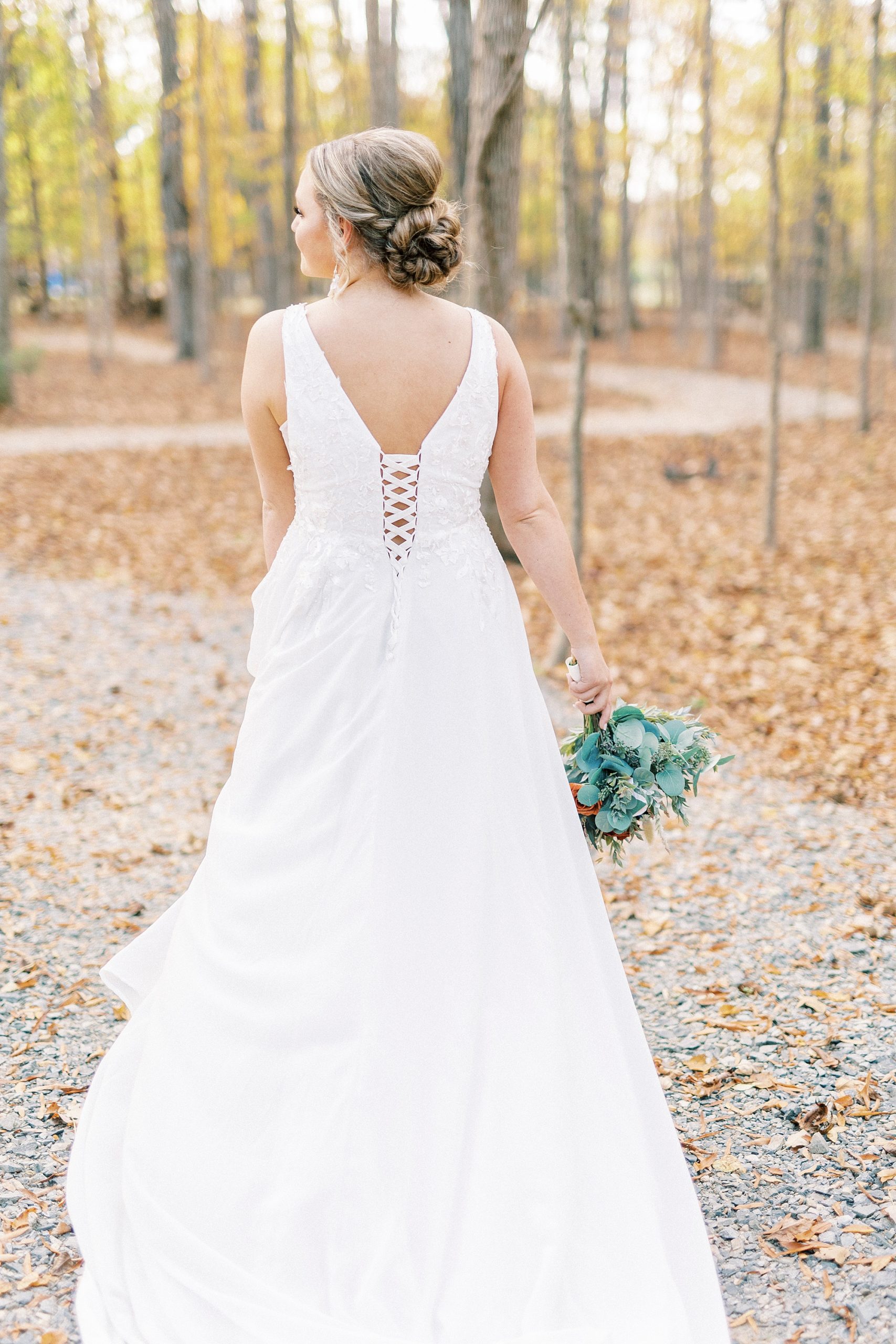 bride walks down path with leaves on it holding bouquet to side 