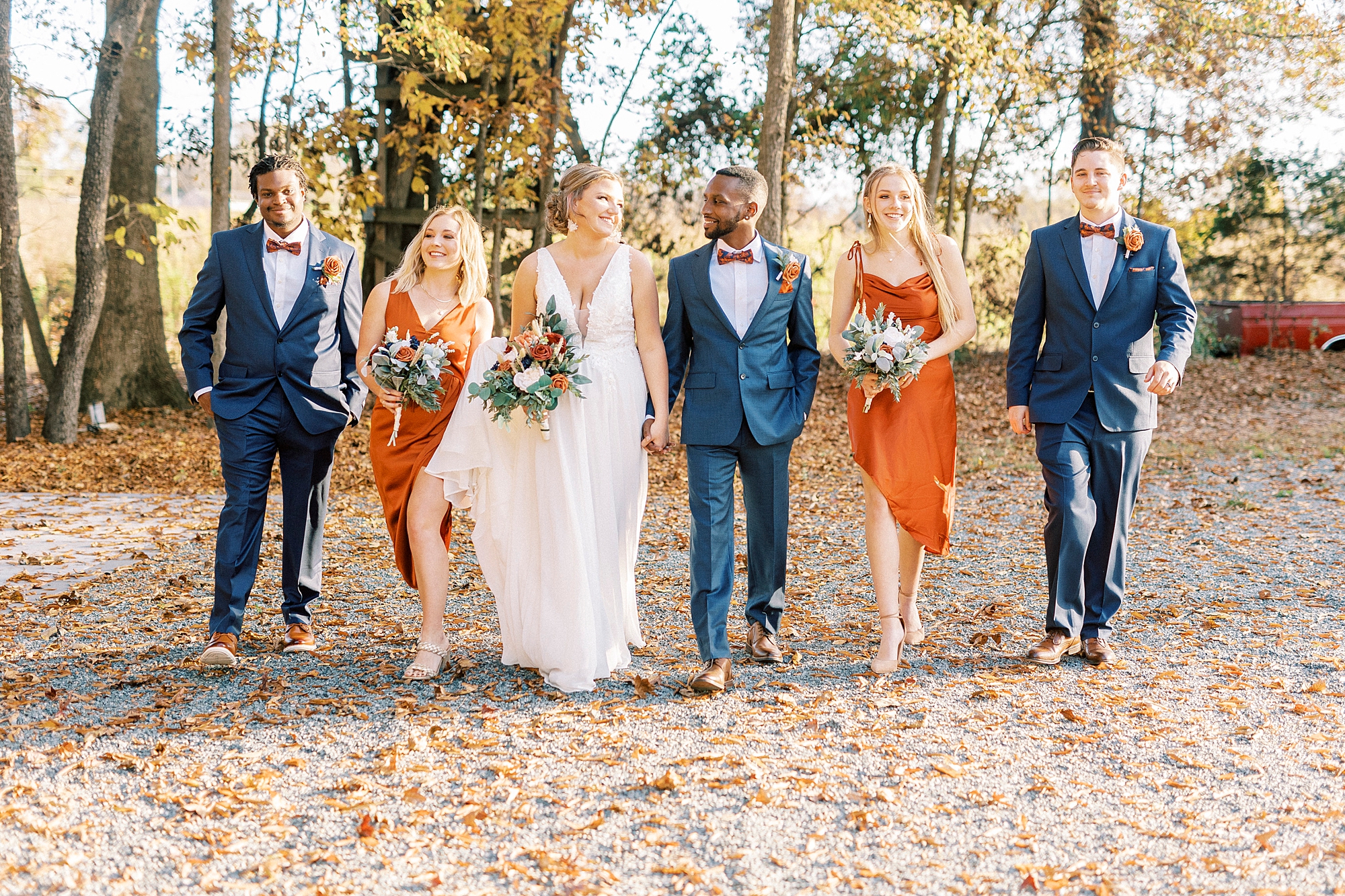 newlyweds walk with wedding party in orange and navy 