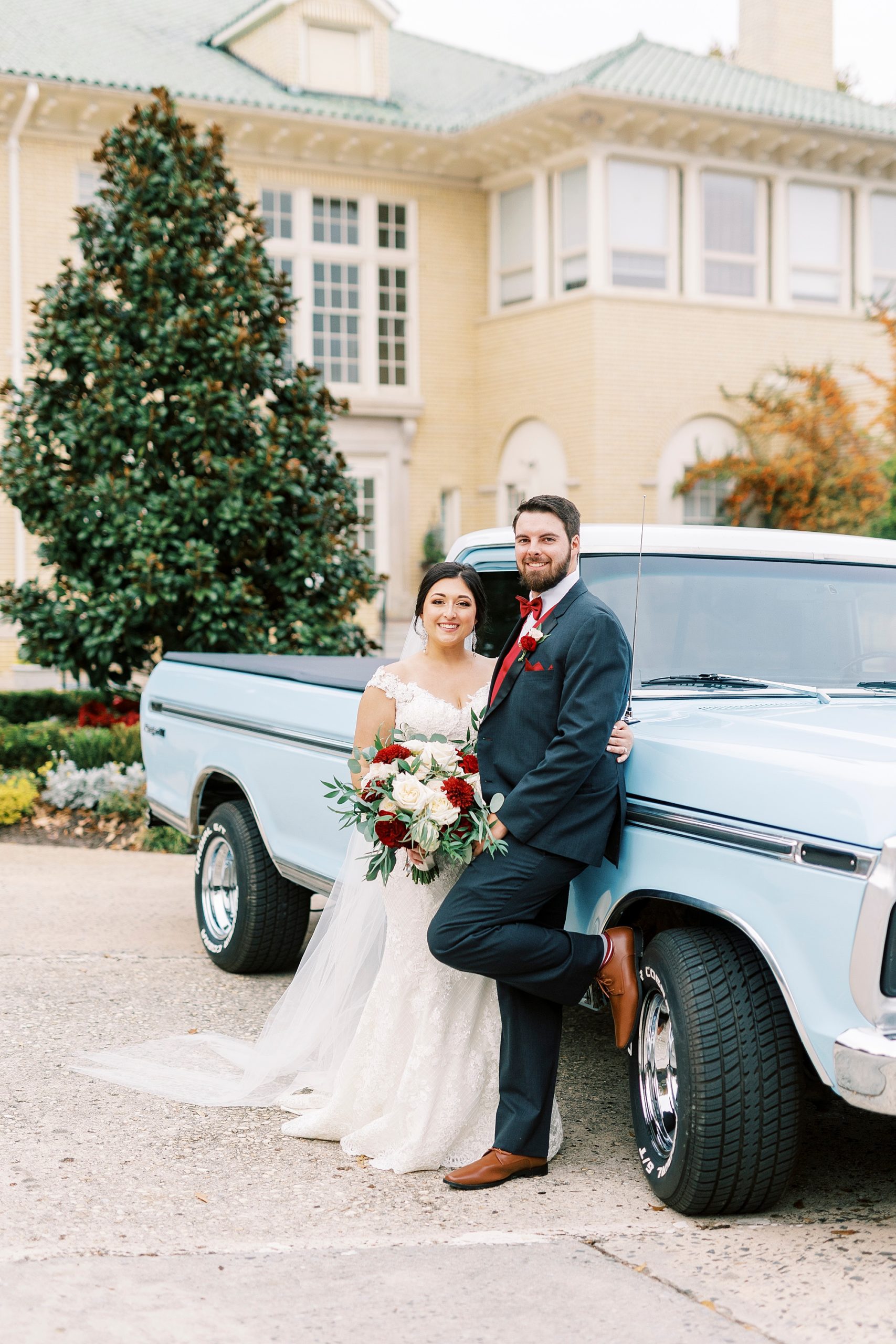 groom leans against resorted blue Ford truck holding bride to him 
