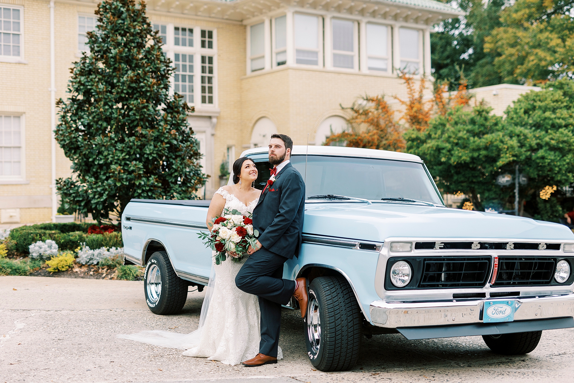 groom leans against resorted blue Ford truck while bride hugs and looks up at him