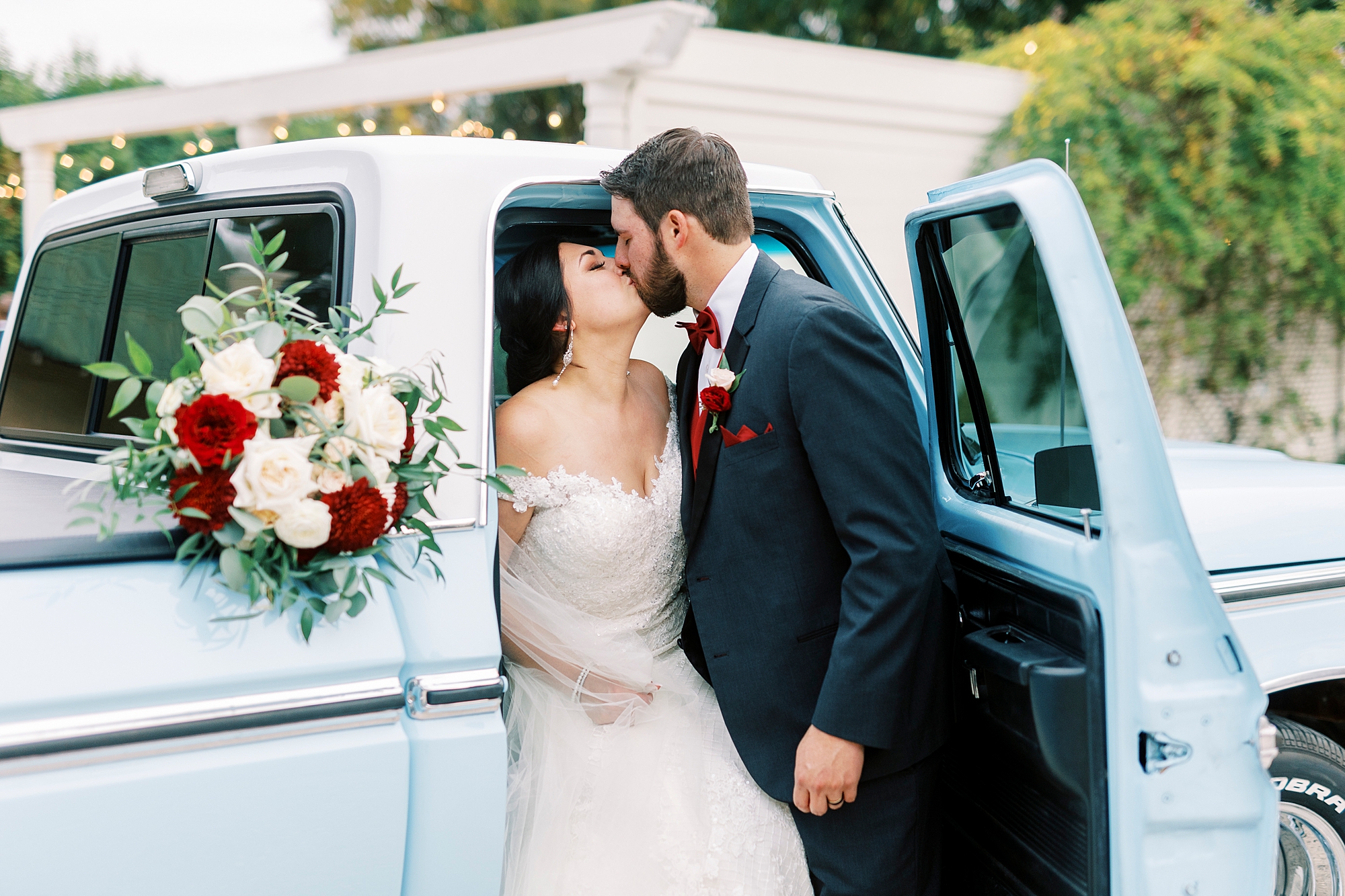 groom leans to kiss bride sitting inside cab of resorted blue Ford truck