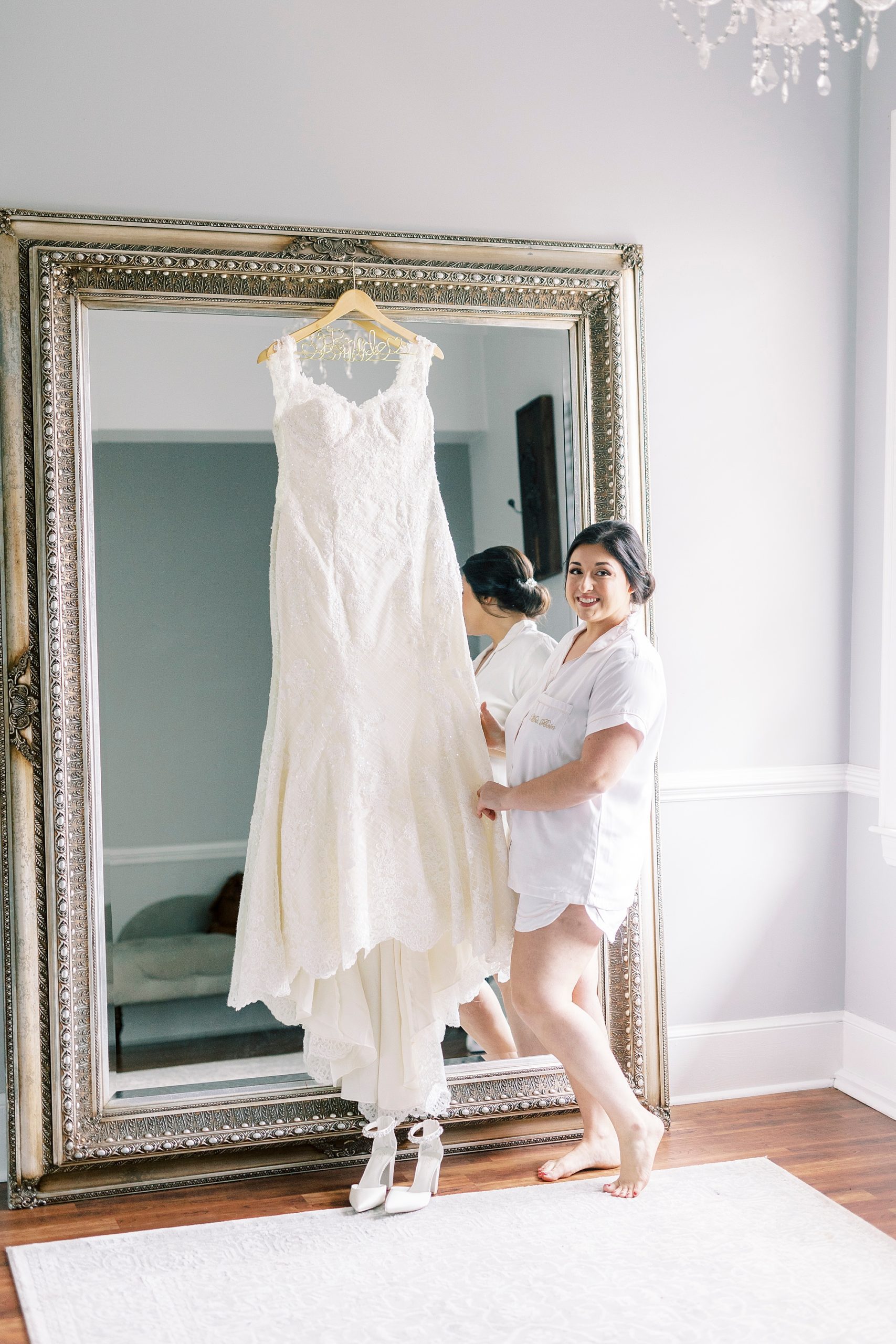 bride stands by wedding gown hanging on mirror in Separk Mansion