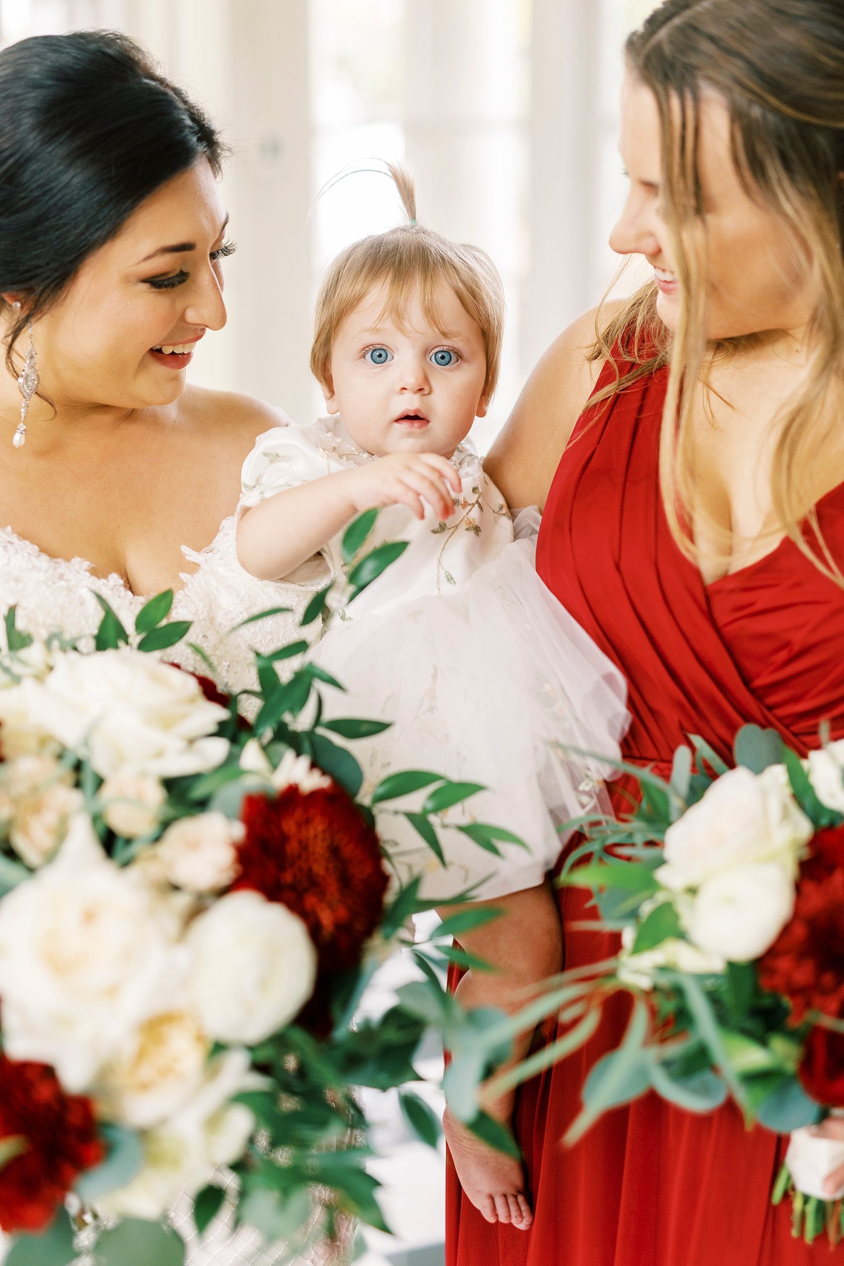 bride smiles with bridesmaid holding flower girl 