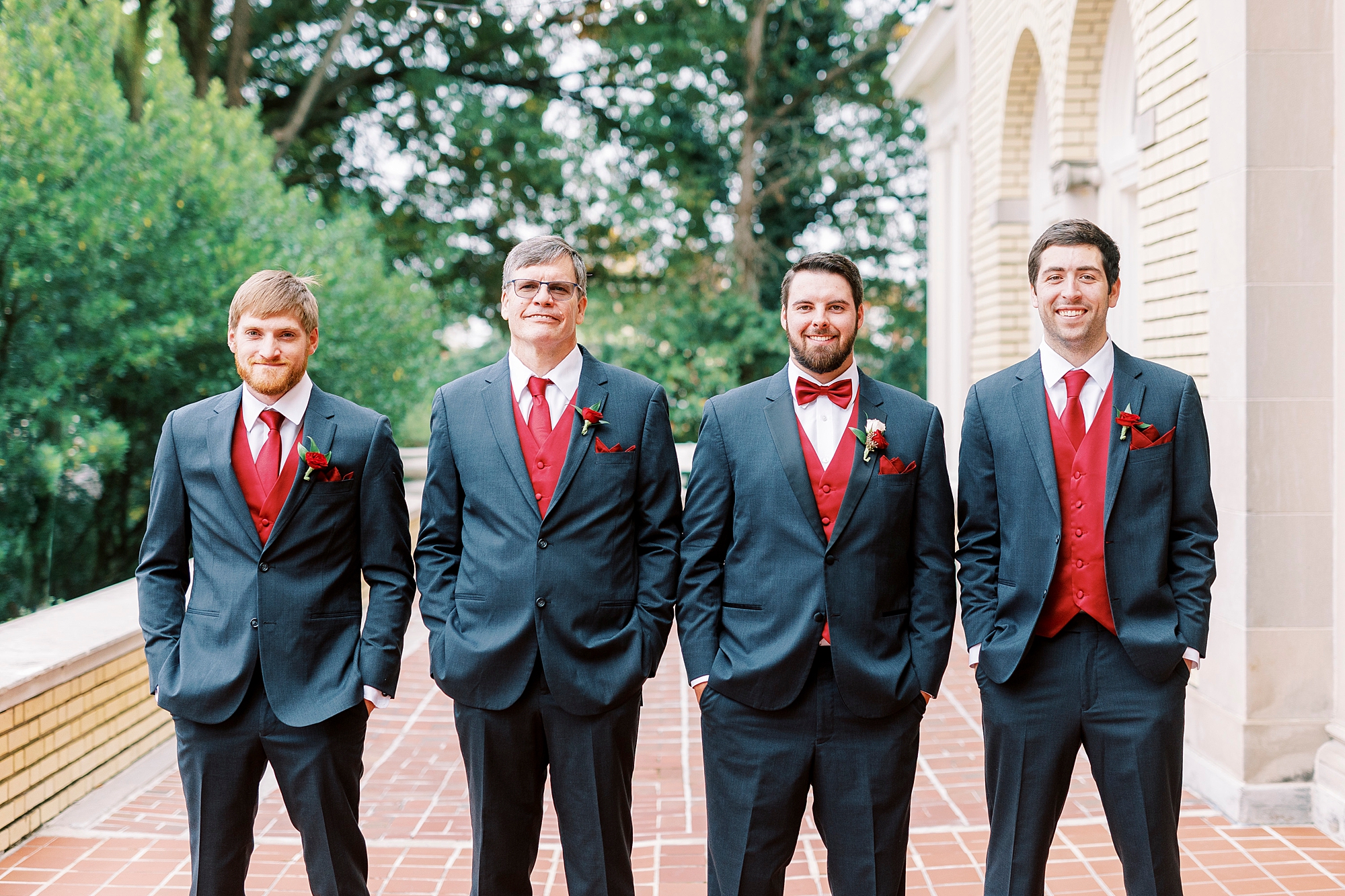 groom stands with groomsmen in navy suits with red vests 