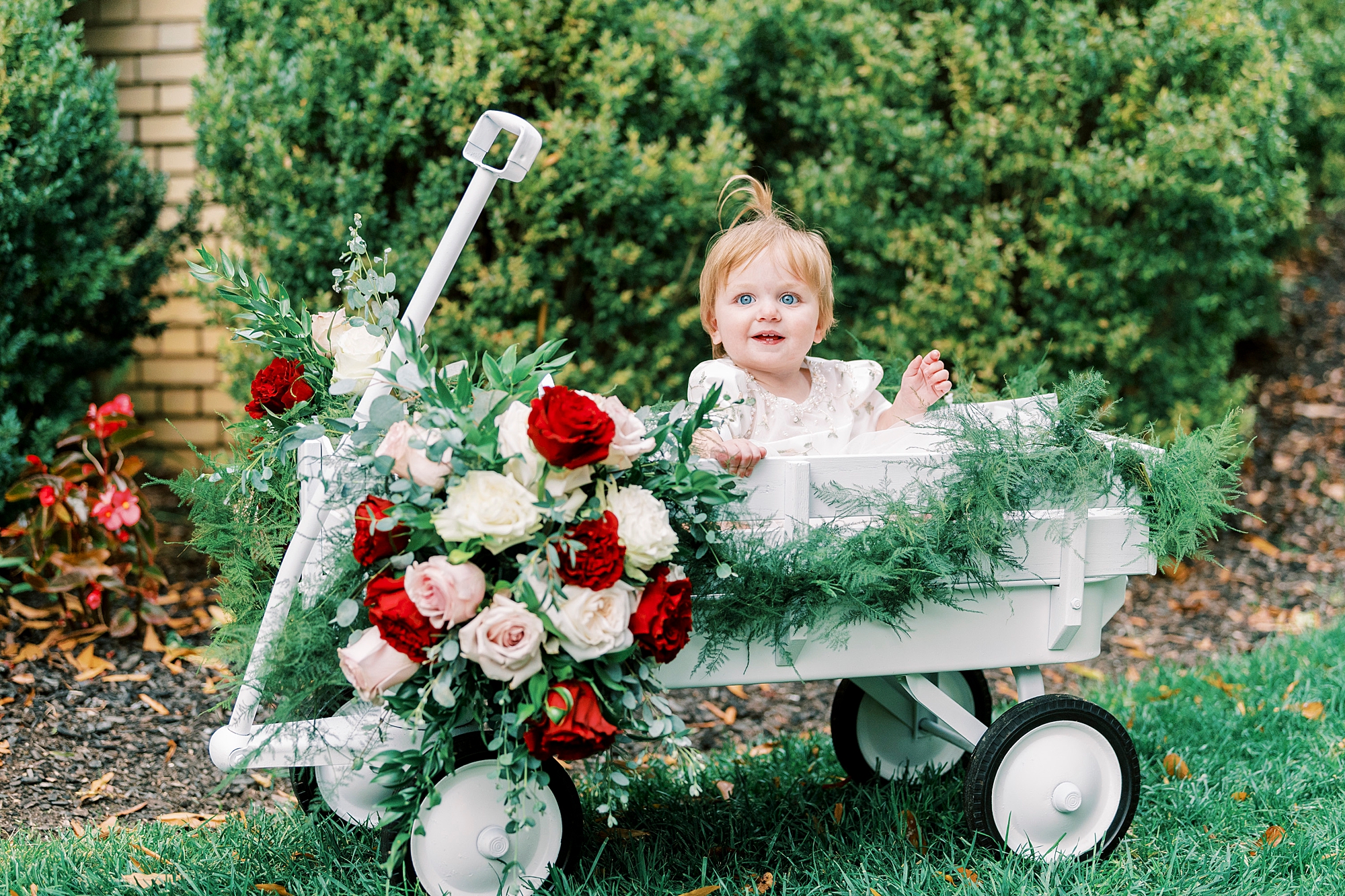flower girl sits in wagon with red and pink flowers