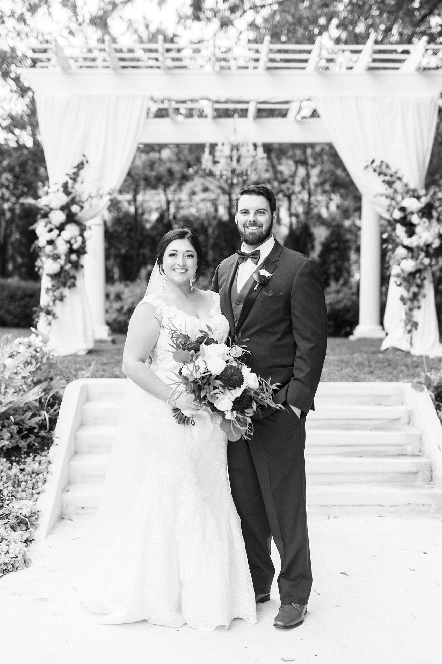 black and white portrait of bride and groom in front of white arbor at Separk Mansion