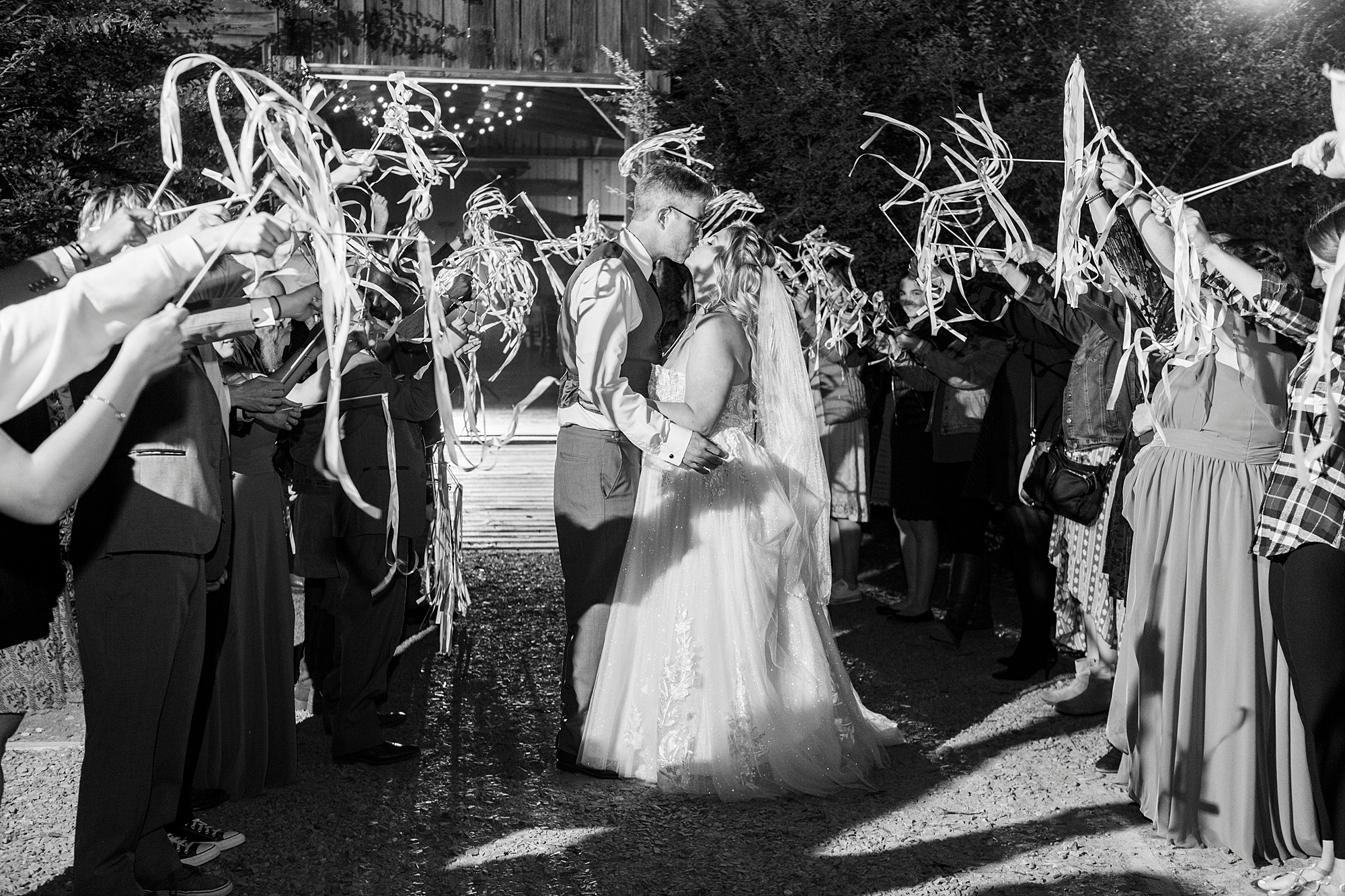 bride and groom kiss during ribbon exit from the Gin at Aw Shucks Farm reception 