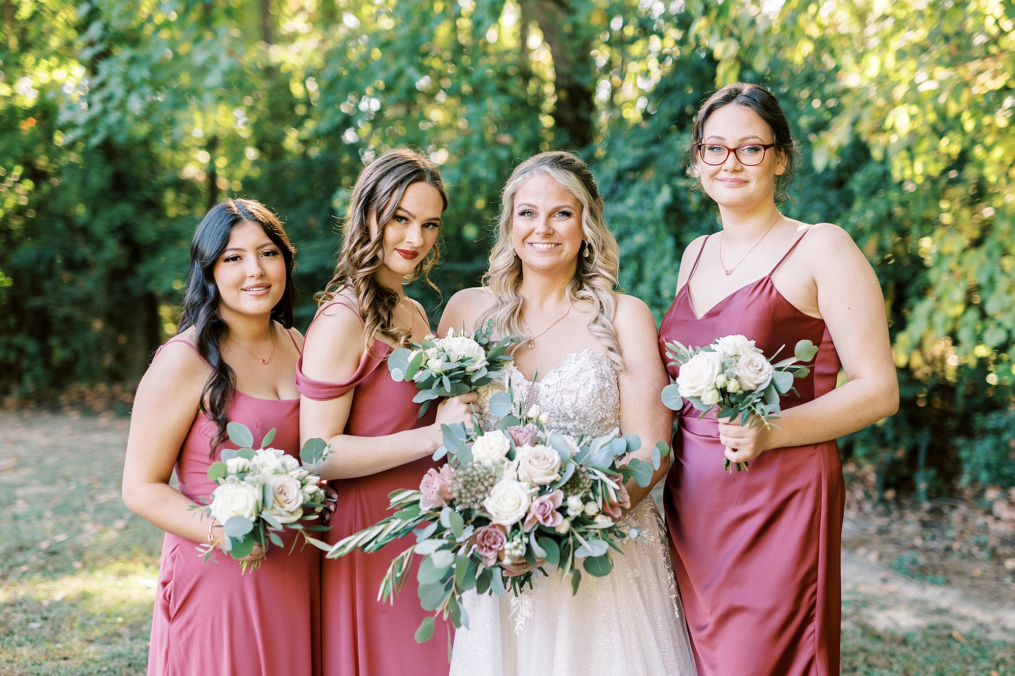 bride poses with three daughters in pink gowns for wedding day