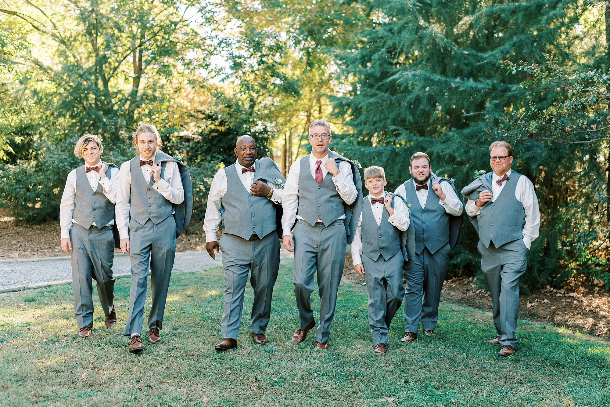 groom walks with groomsmen in grey vests and jackets over shoulders 