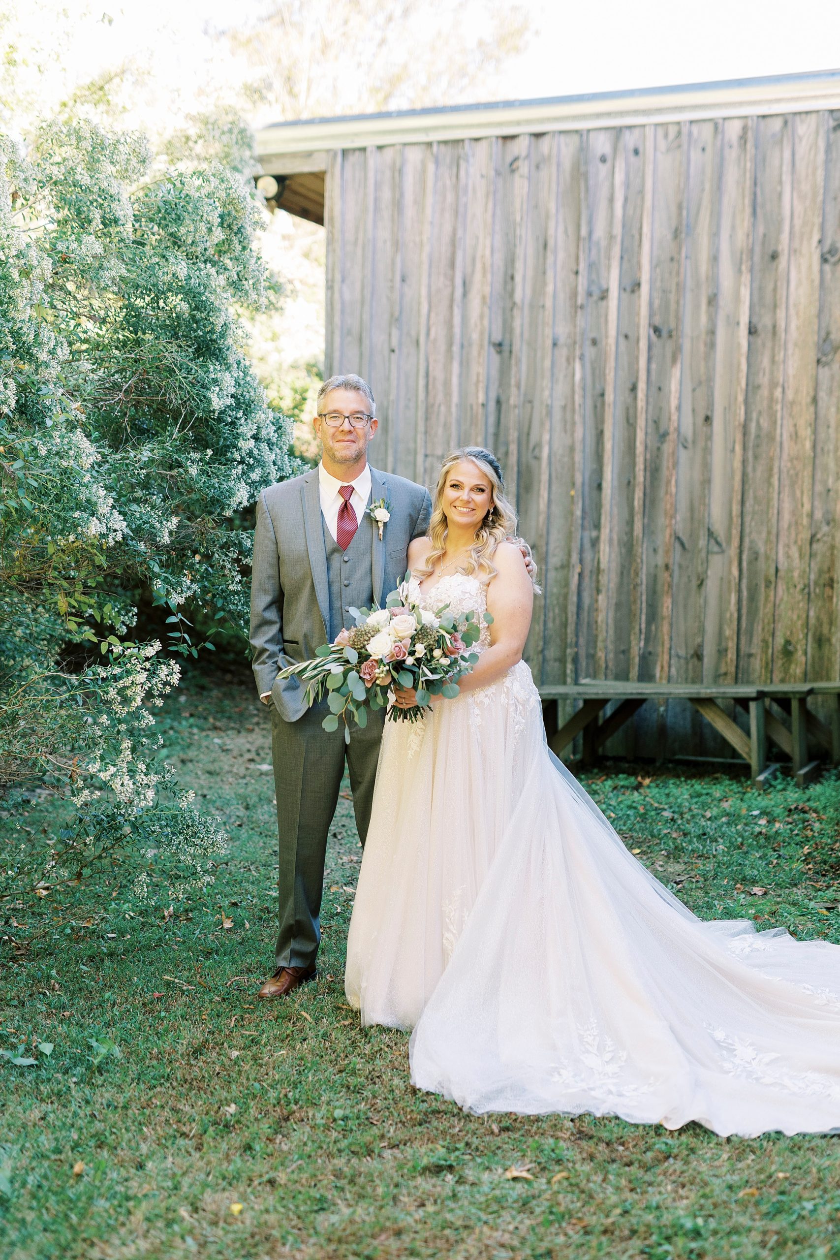 bride and groom stand side by side in front of wooden barn at the Gin at Aw Shucks Farm