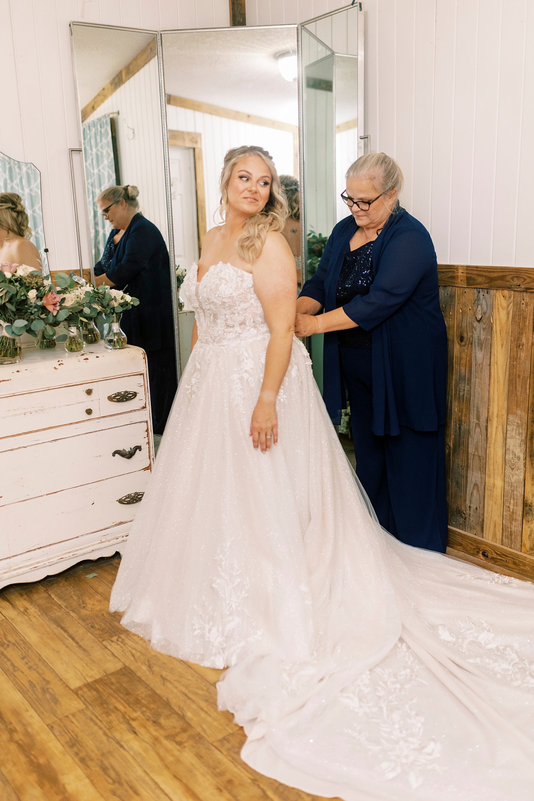 mother helps bride into wedding gown at the Gin at Aw Shucks Farm