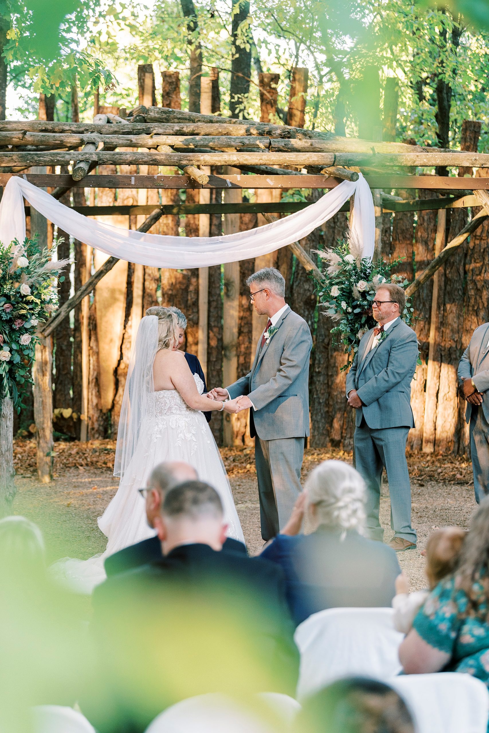 bride and groom exchange vows under wooden arbor at the Gin at Aw Shucks Farm