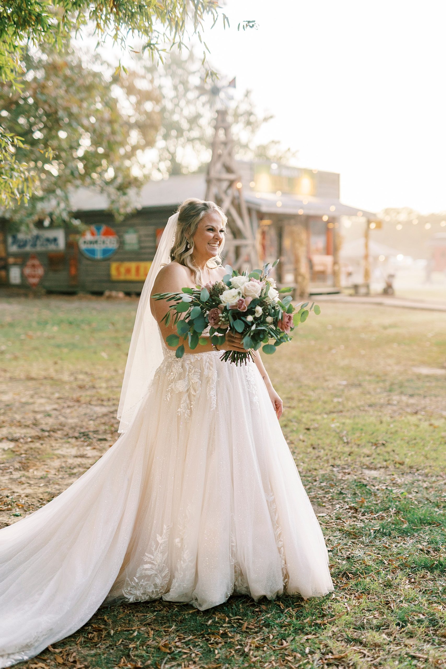 bride smiles holding bouquet at sunset in front of barn at the Gin at Aw Shucks Farm
