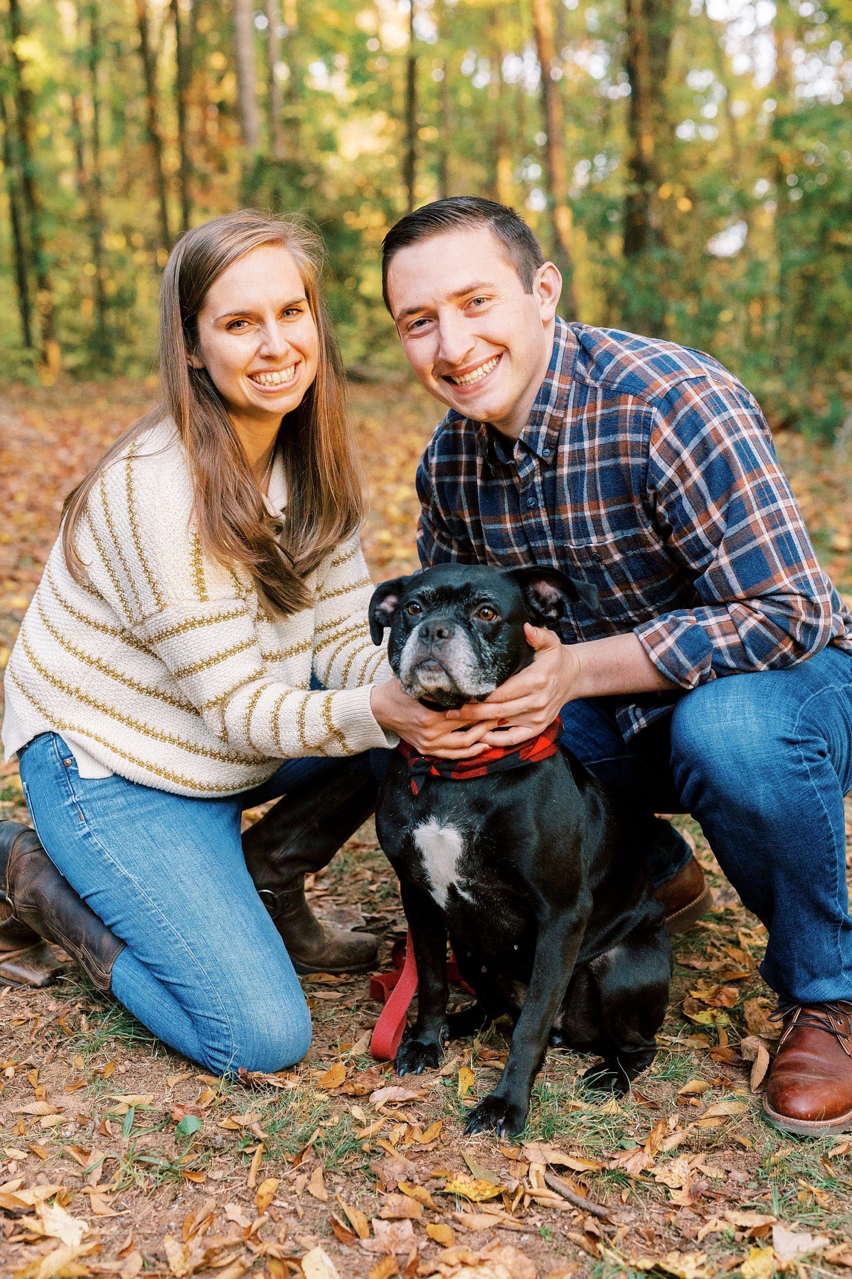 bride and groom sit together with dog during fall Latta Nature Preserve engagement session