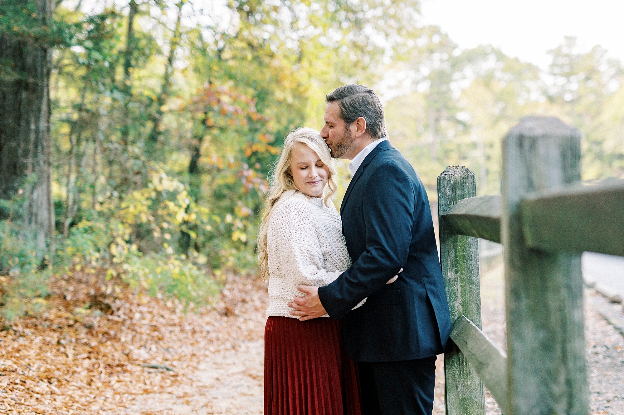 groom leans to kiss bride alongside wooden fence at Latta Nature Preserve