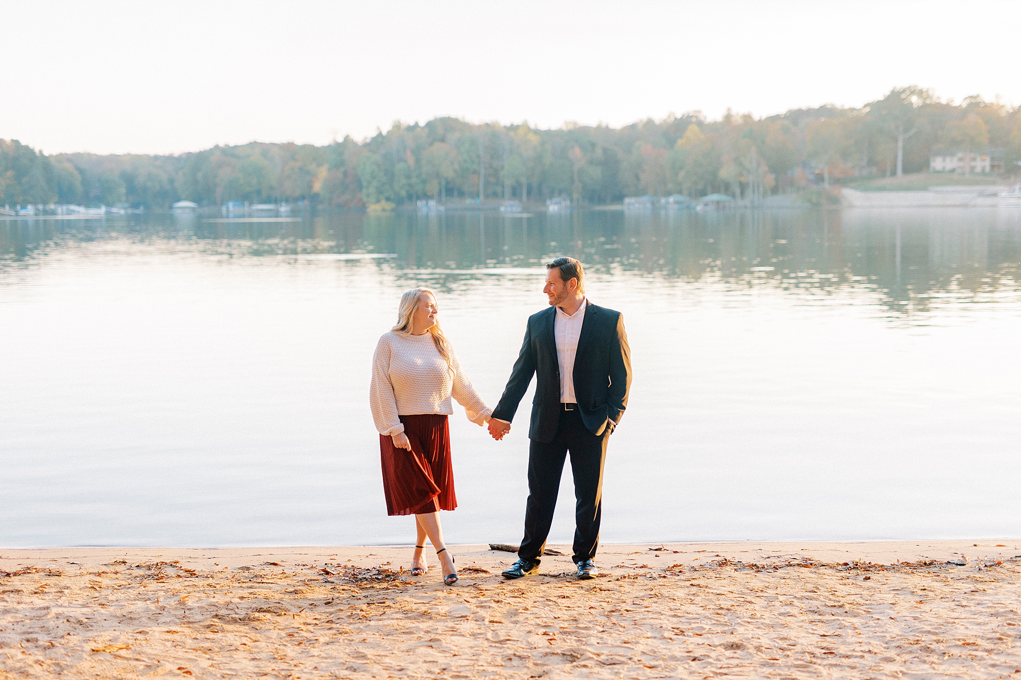 engaged couple holds hands on beach by water at Latta Nature Preserve