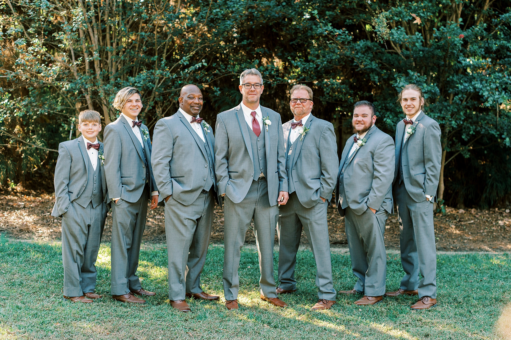 groom stands with groomsmen in grey suits at the Gin at Aw Shucks Farm