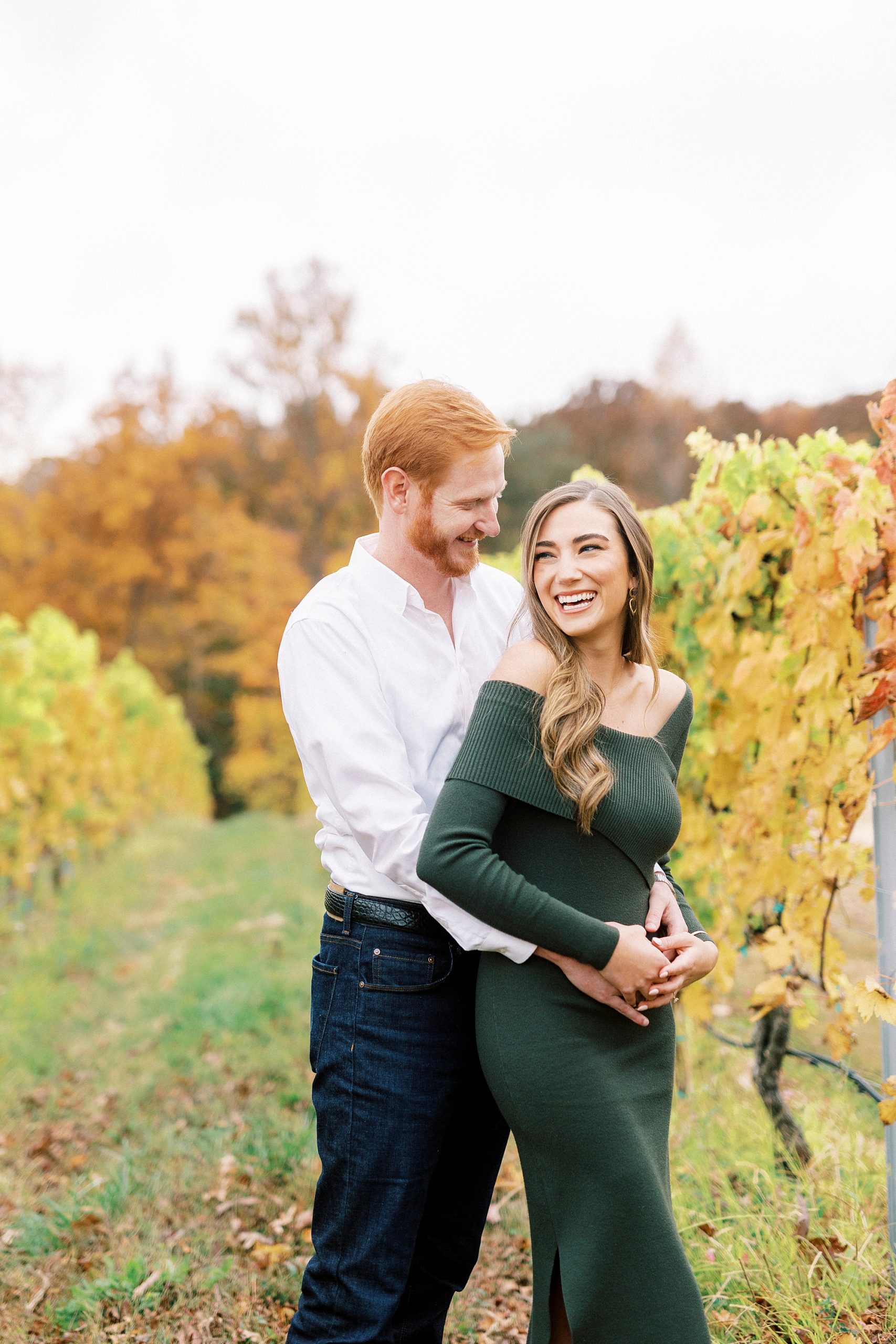 man hugs woman from behind making her laugh in the vines at Raffaldini Vineyards