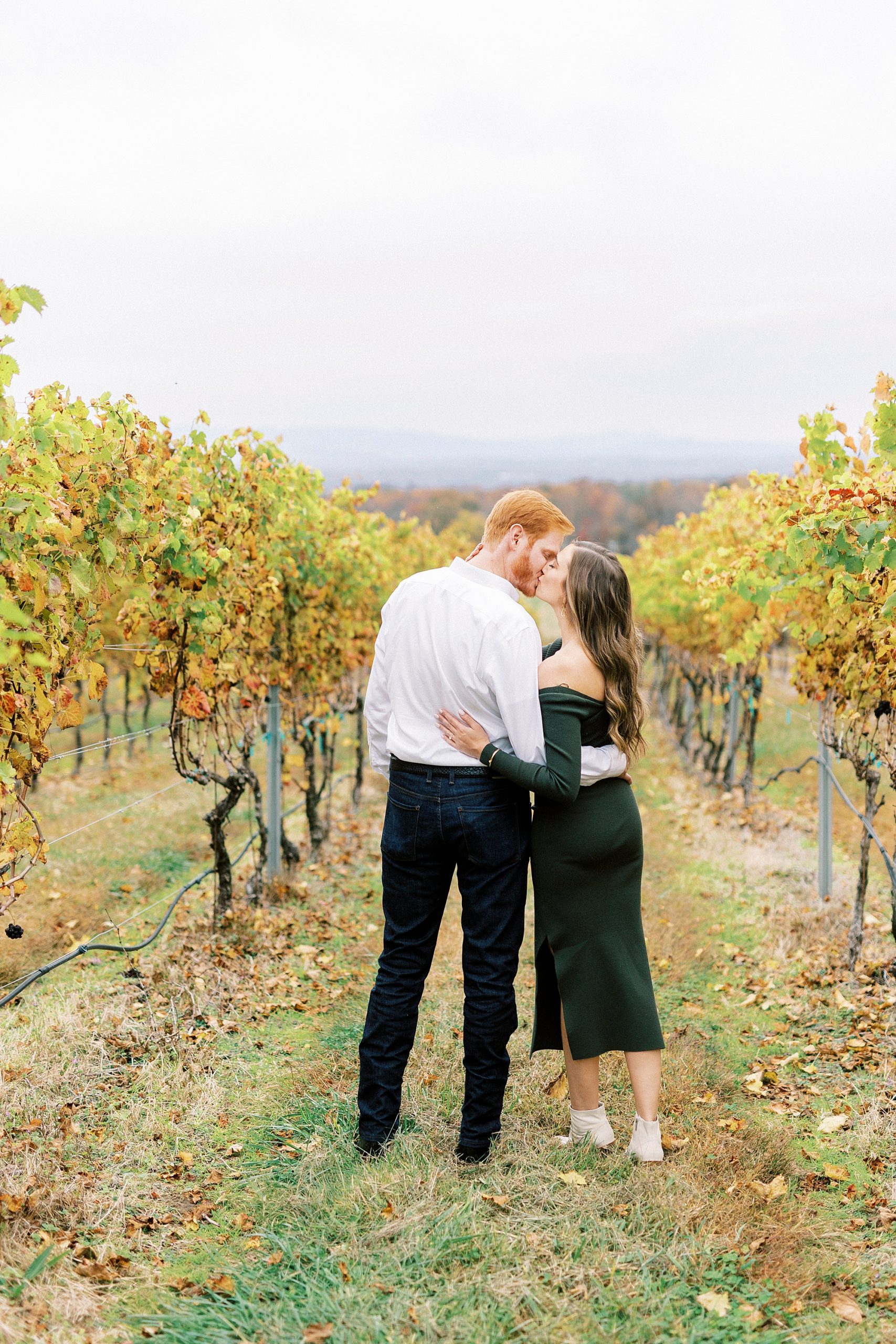 engaged couple leans together between vines at Raffaldini Vineyards