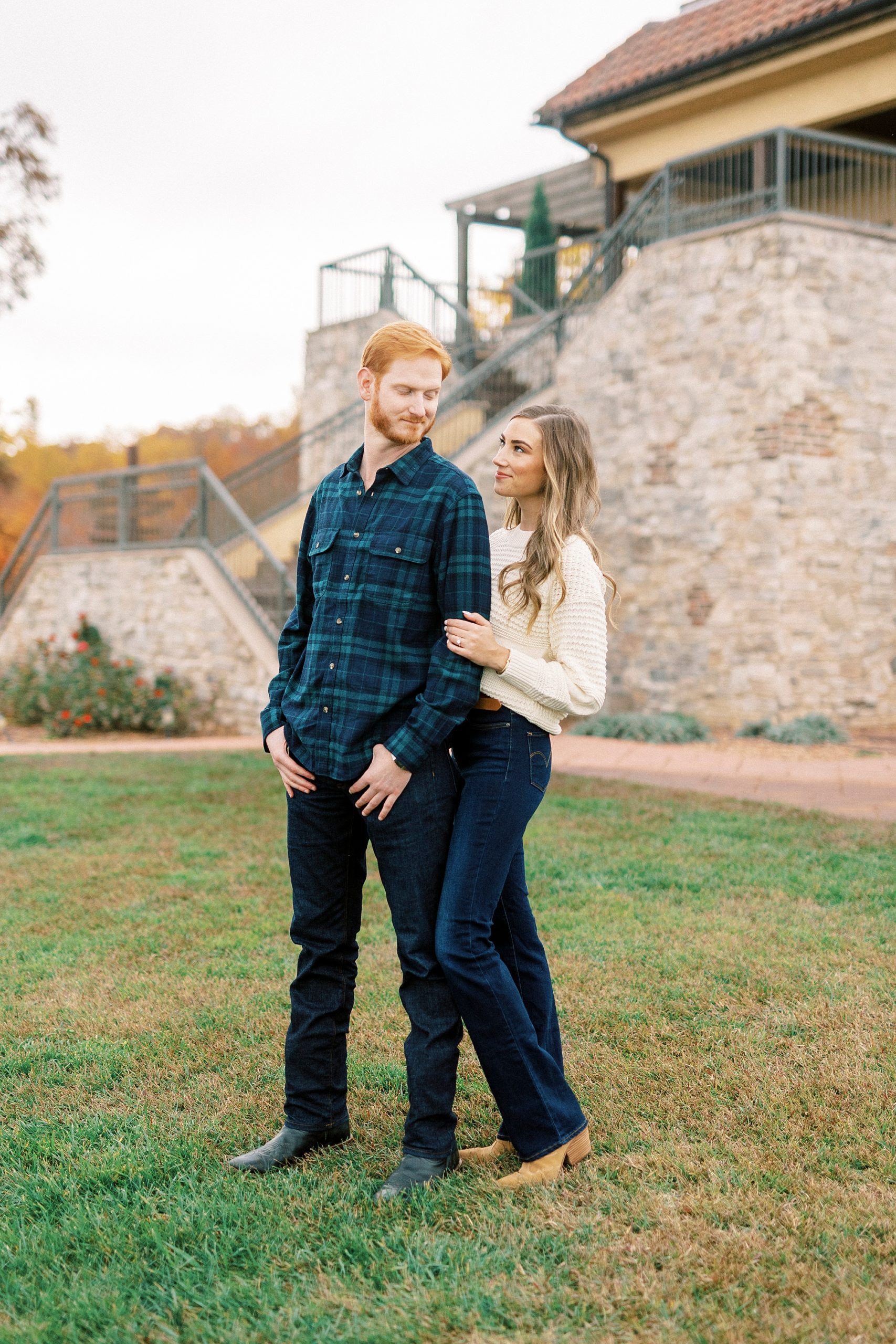 woman stands behind man holding his arm during fall engagement session 