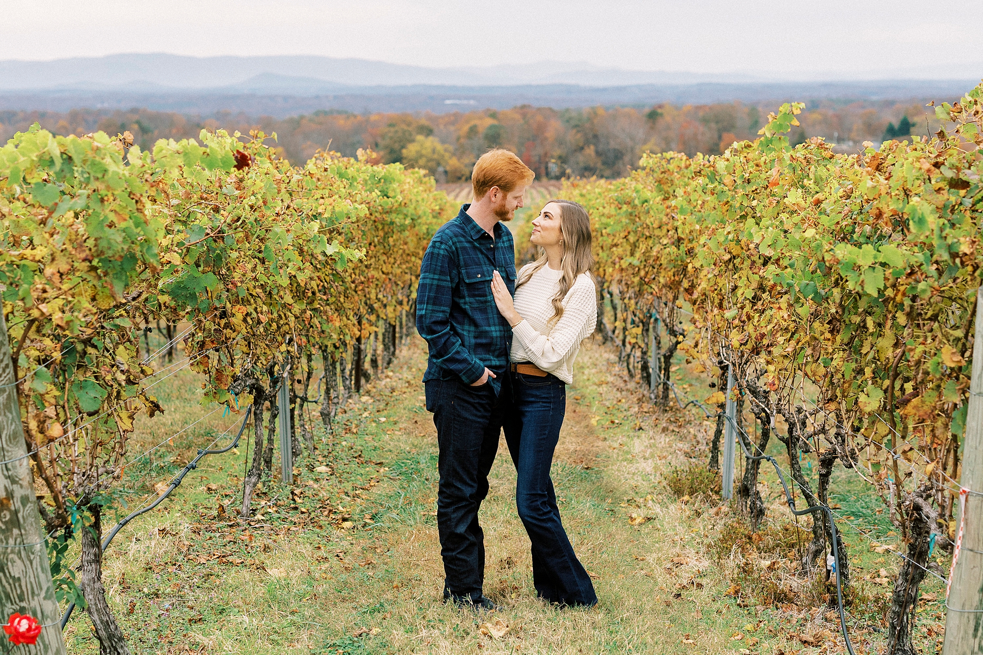 couple smiles together between vines in front of mountains at Raffaldini Vineyards