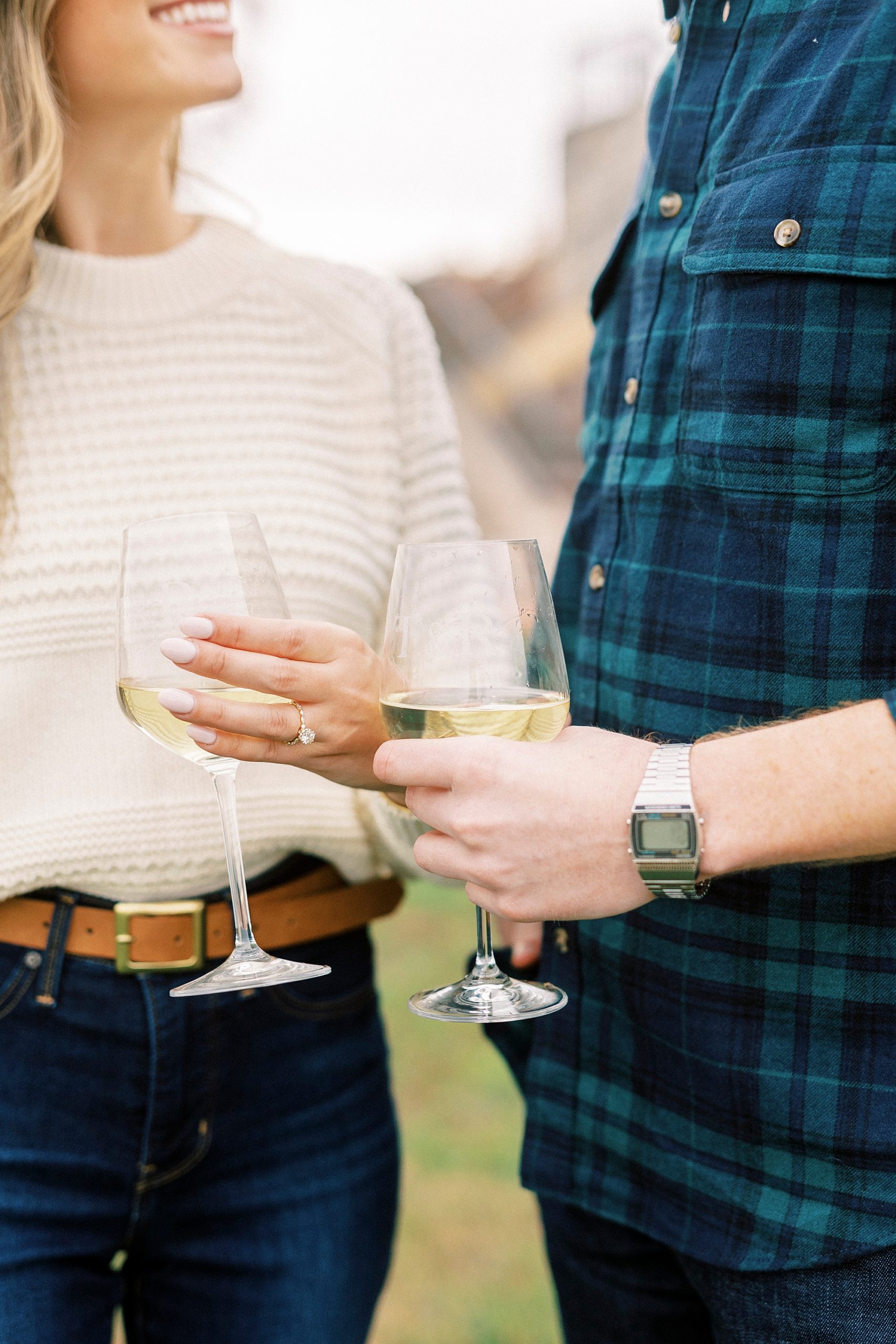 engaged couple holds glasses of white wine together 