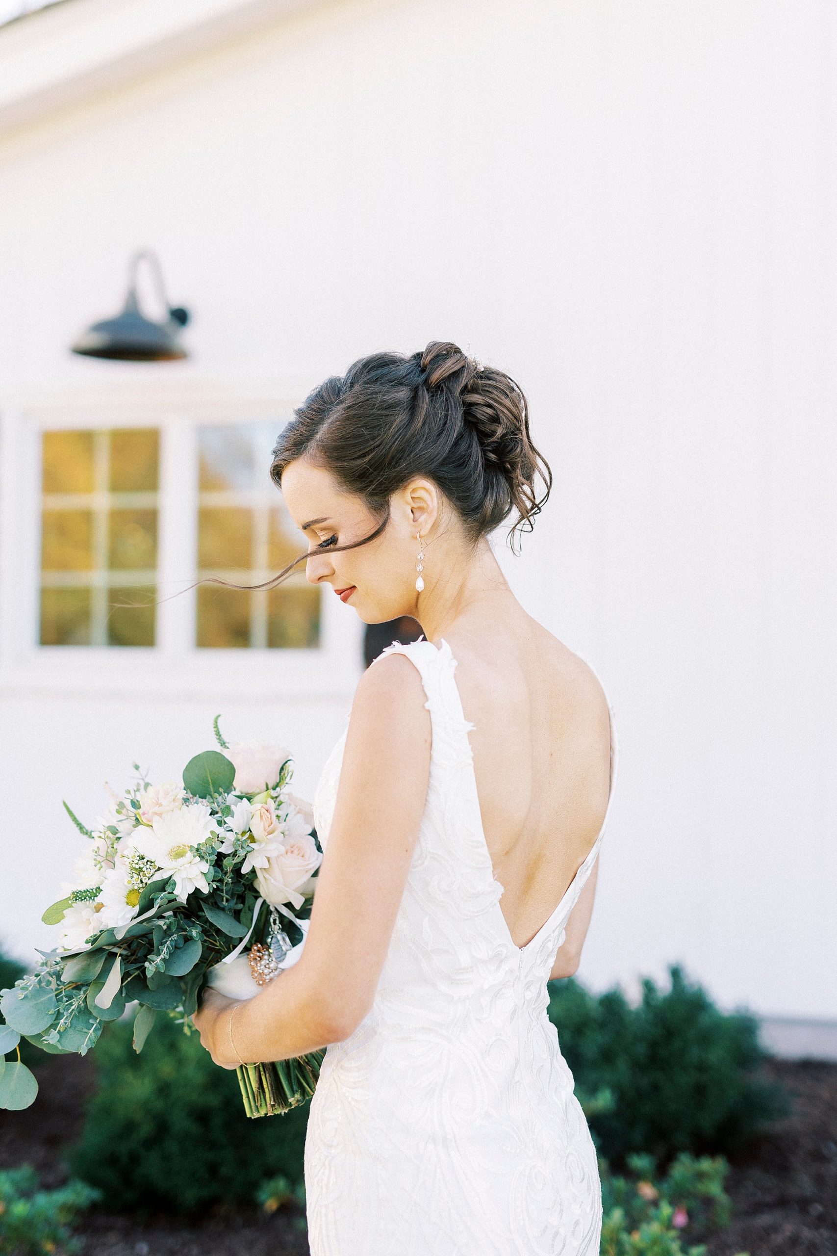 bride holds bouquet by white wall at Chickadee Hill Farms